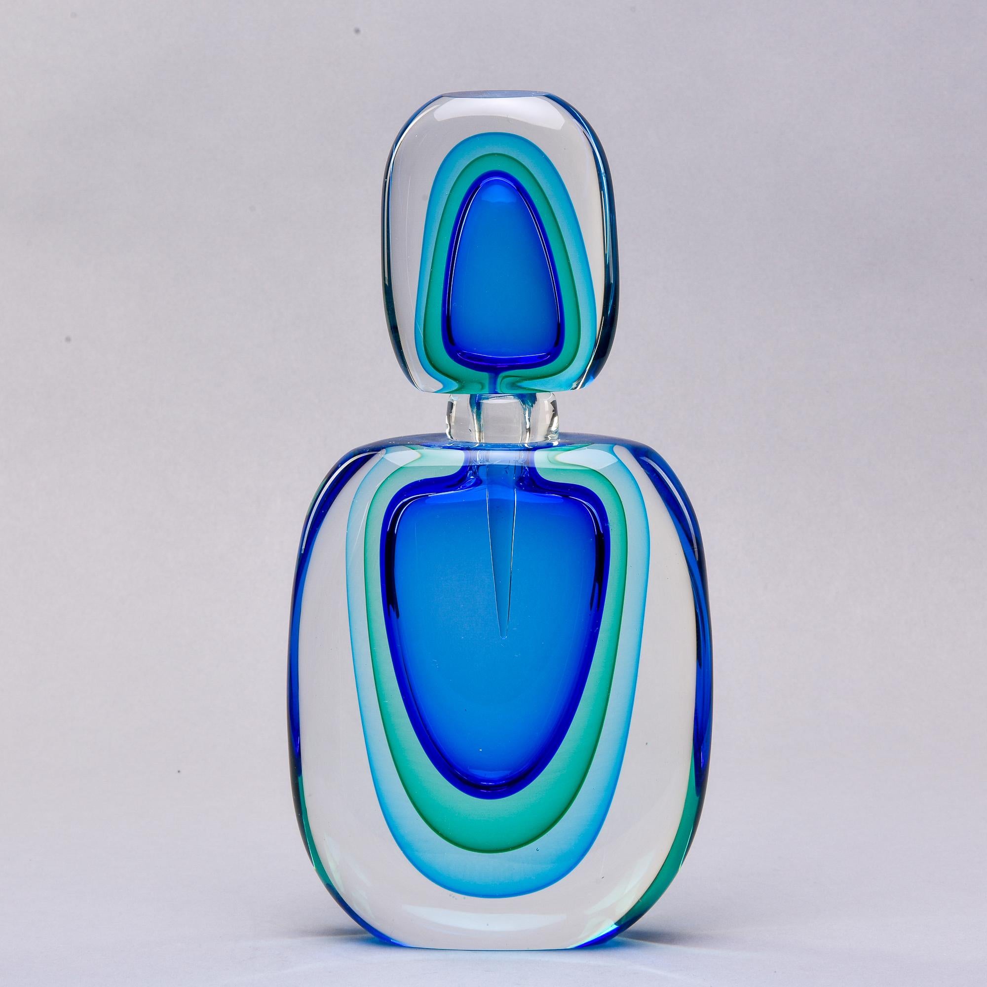 New oversized Murano glass perfume bottle stands 14” tall. Done in sommerso style with layers of blue and green toned glass submerged in heavy clear glass. Coordinated stopper has an attached scent dabber. Unsigned - unknown Murano maker. At the