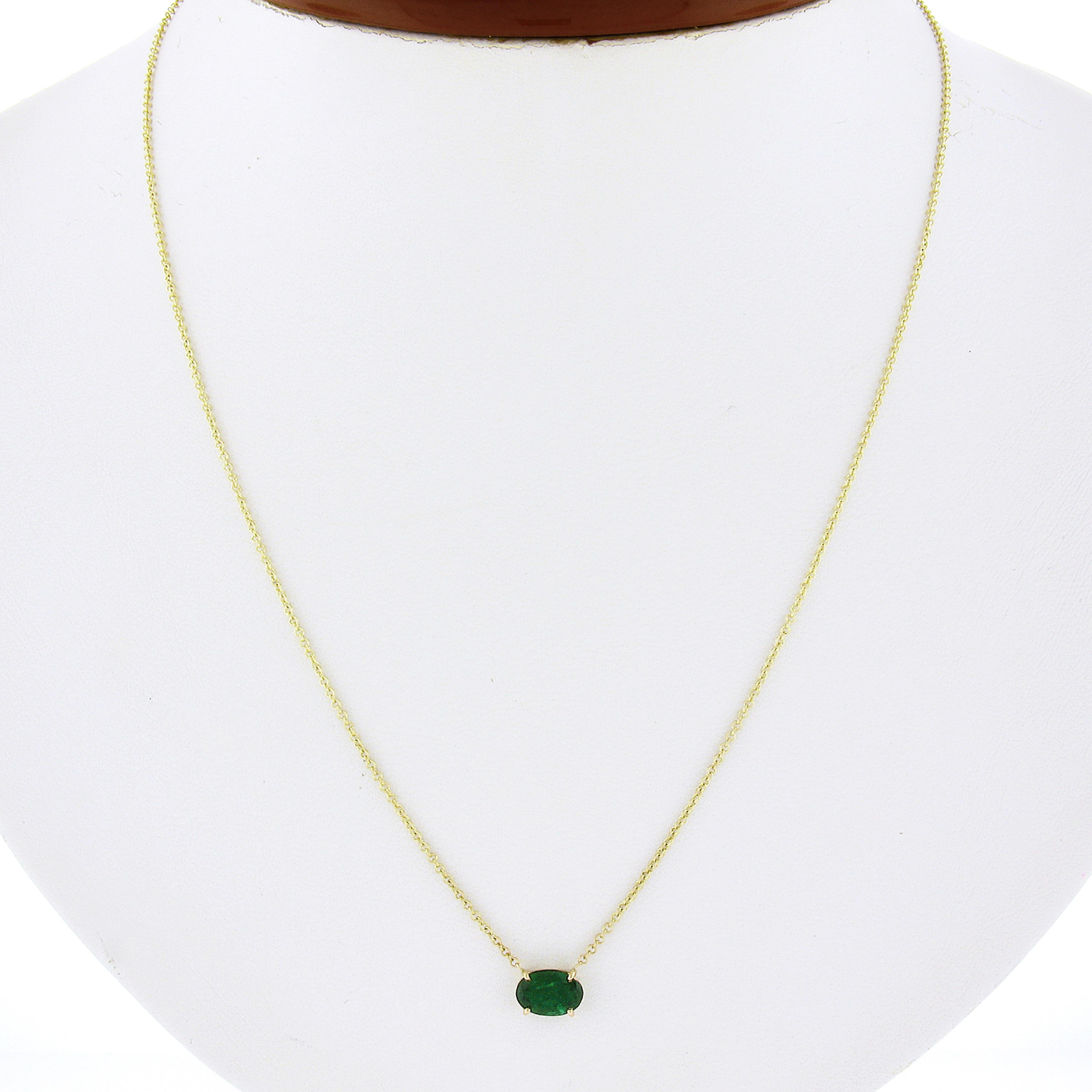 This amazing petite solitaire pendant necklace is newly crafted in solid 14k yellow gold and features a very fine natural emerald gemstone that is neatly prong set in a sturdy basket setting at the center. This gorgeous stone is oval cut and set