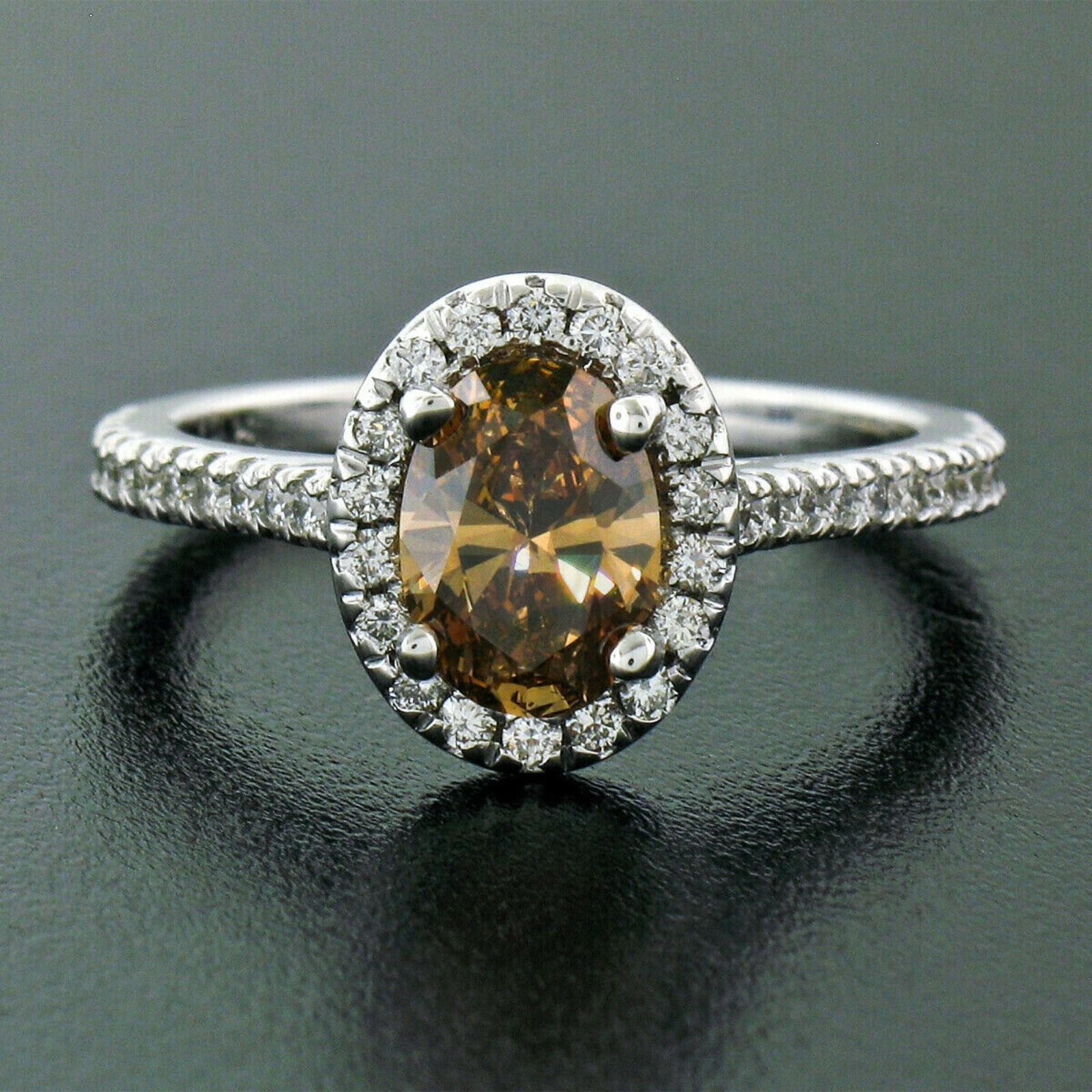 This gorgeous diamond engagement ring is newly crafted in solid 14k white gold and features an amazing, 1.00 carat, GIA certified oval brilliant cut diamond prong set at its center. The center stone is a natural, fancy brown-orange color and is very