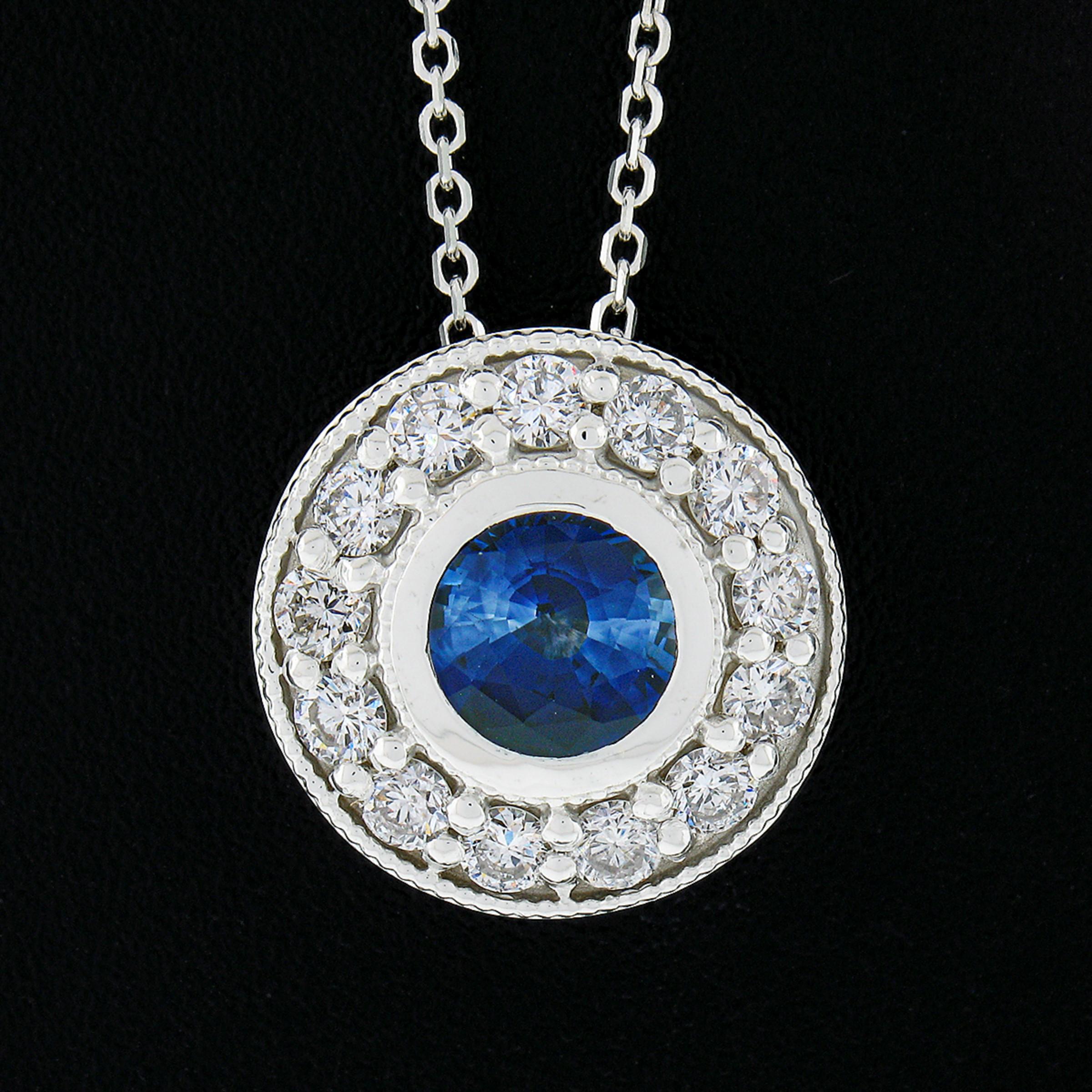 This stunning pendant necklace is newly crafted in solid 14k white gold and features a gorgeous sapphire neatly bezel set at the center of a fine diamond halo. The round brilliant cut sapphire is an attractive size, weighing exactly 1.11 carats, and