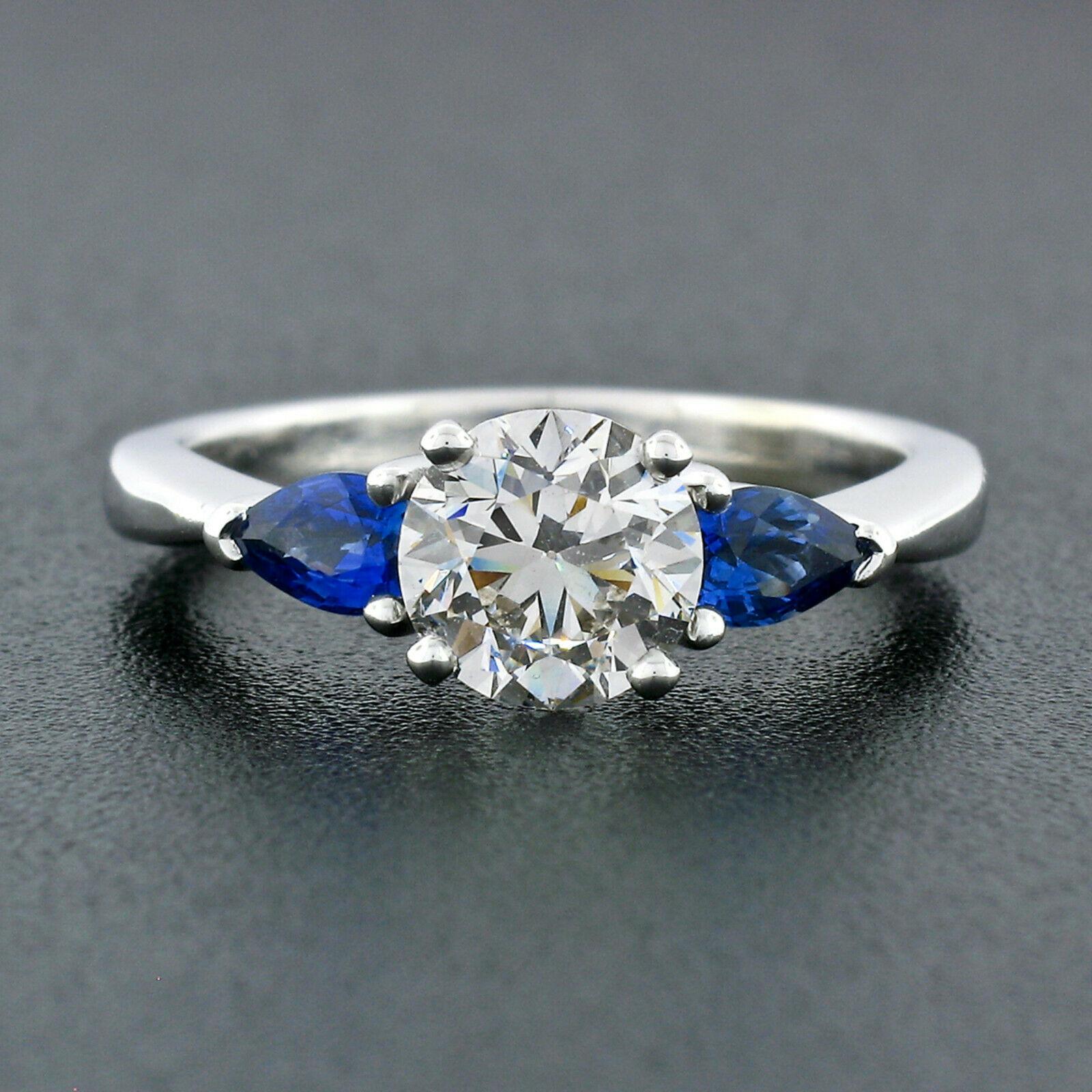 You are looking at a magnificent diamond and sapphire three-stone engagement ring that is newly crafted from solid 14k white gold. This ring features a stunning, GIA certified, round brilliant diamond solitaire prong set at its center. The diamond