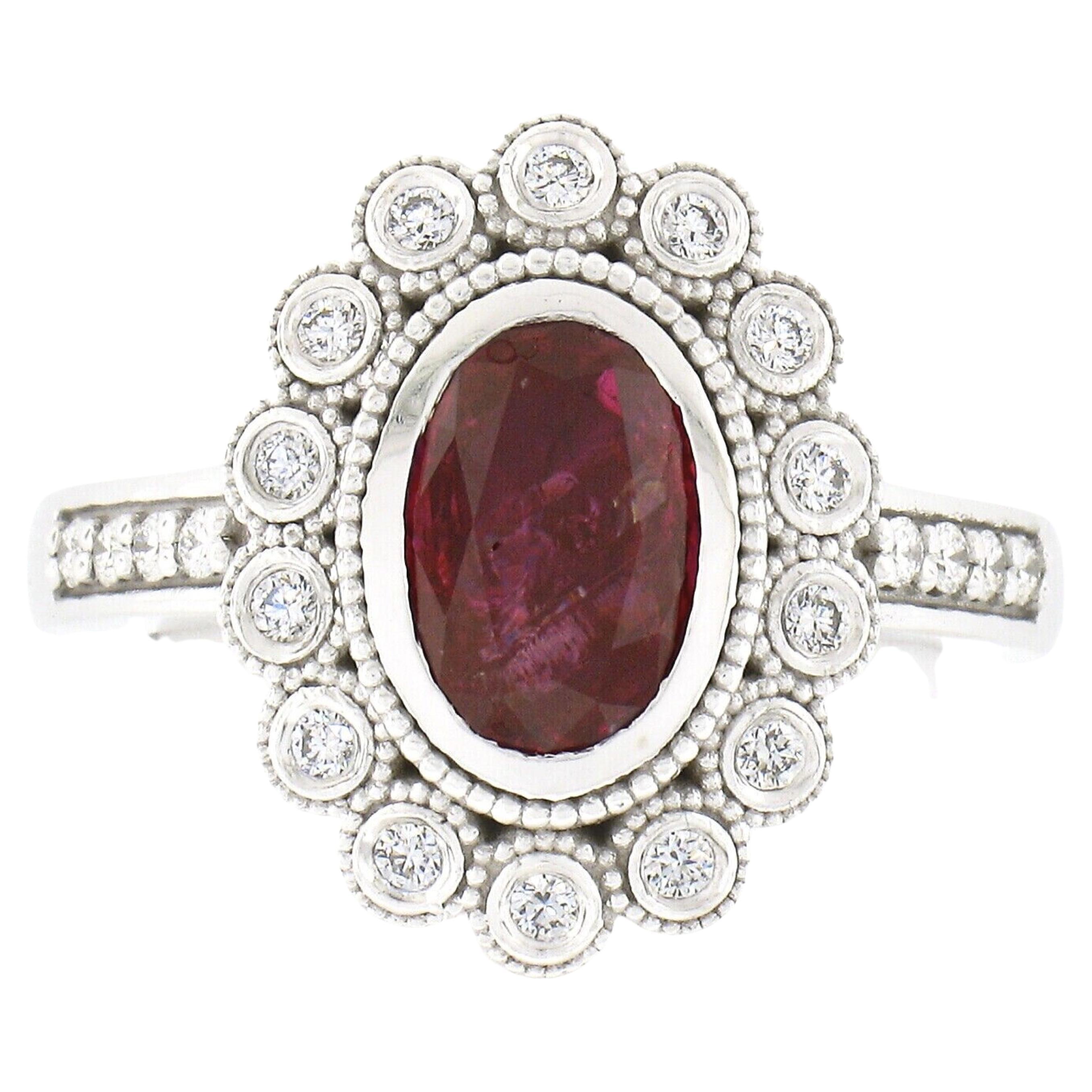 Aquí tenemos un anillo de compromiso o para la mano derecha totalmente nuevo y diseñado a medida, fabricado en oro blanco macizo de 14 quilates, con un rubí absolutamente impresionante y un halo de diamantes. El rubí ovalado de talla brillante,