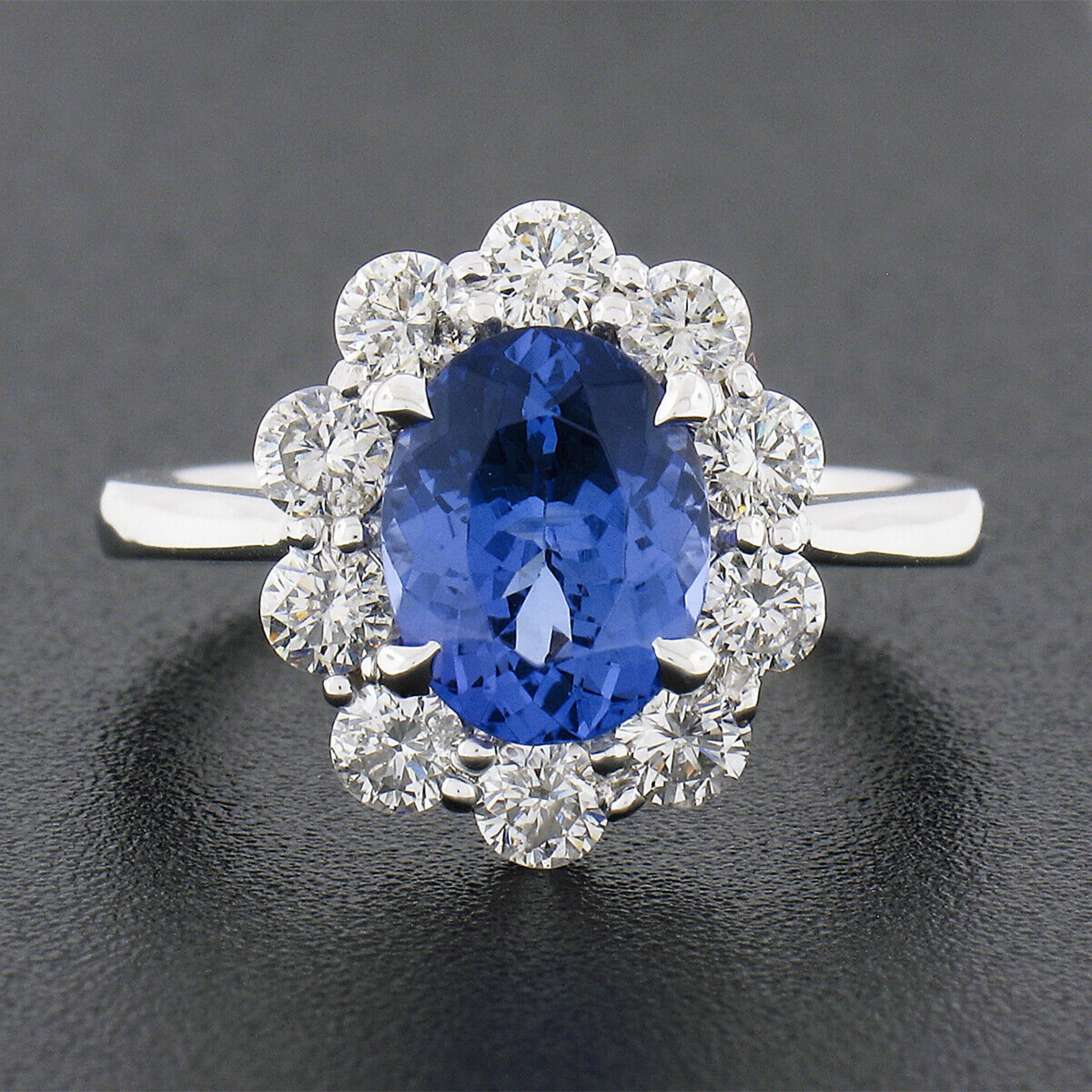 This magnificent tanzanite and diamond engagement ring is newly crafted from solid 14k white gold and features a gorgeous blueish violet tanzanite prong set at its center. The tanzanite is oval brilliant cut and weighs exactly 1.87 carats.