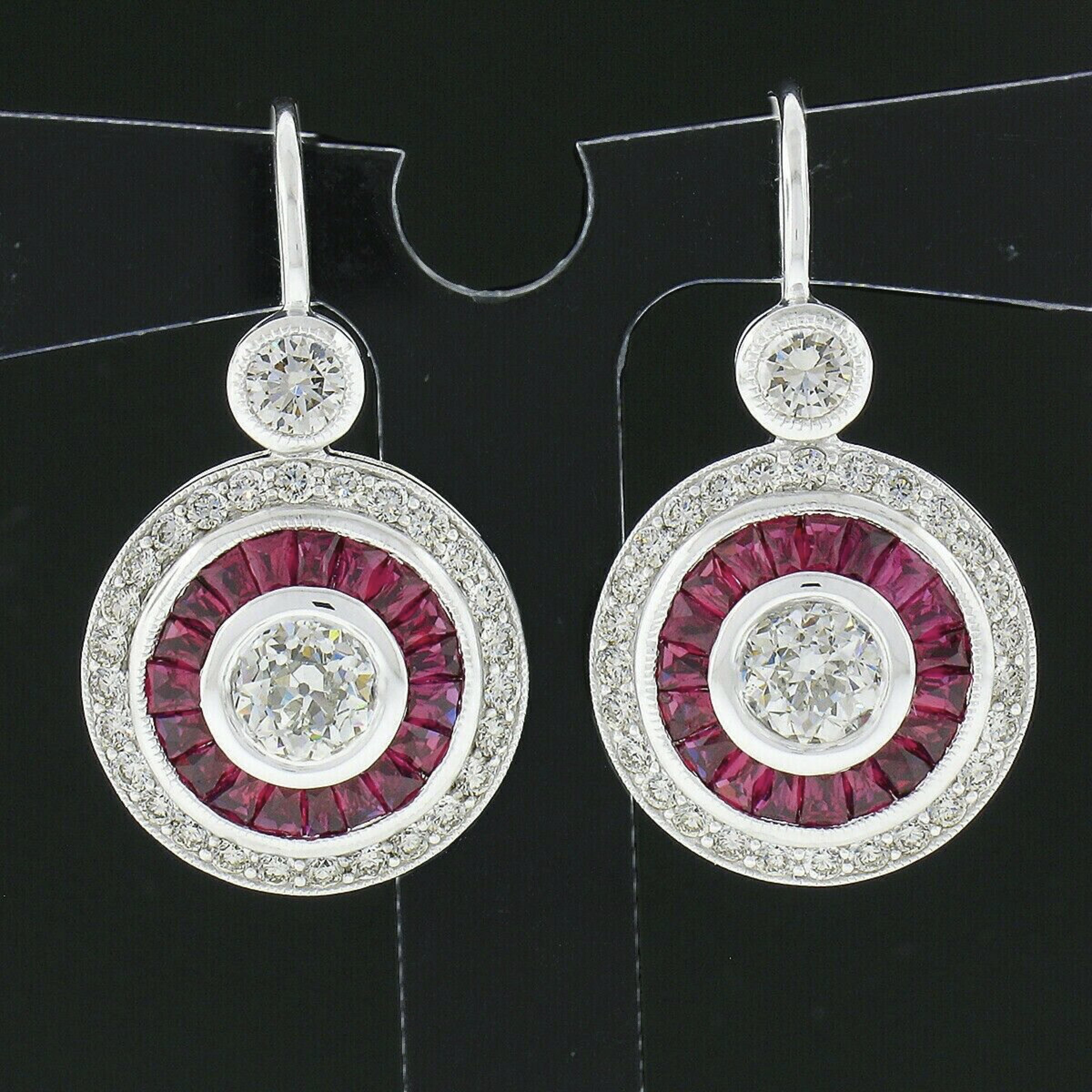 This spectacular and very well made pair of drop earrings is newly crafted in solid 14k white gold and feature two antique, old European cut, diamonds that are neatly bezel set at their center and further surrounded by gorgeous natural rubies and