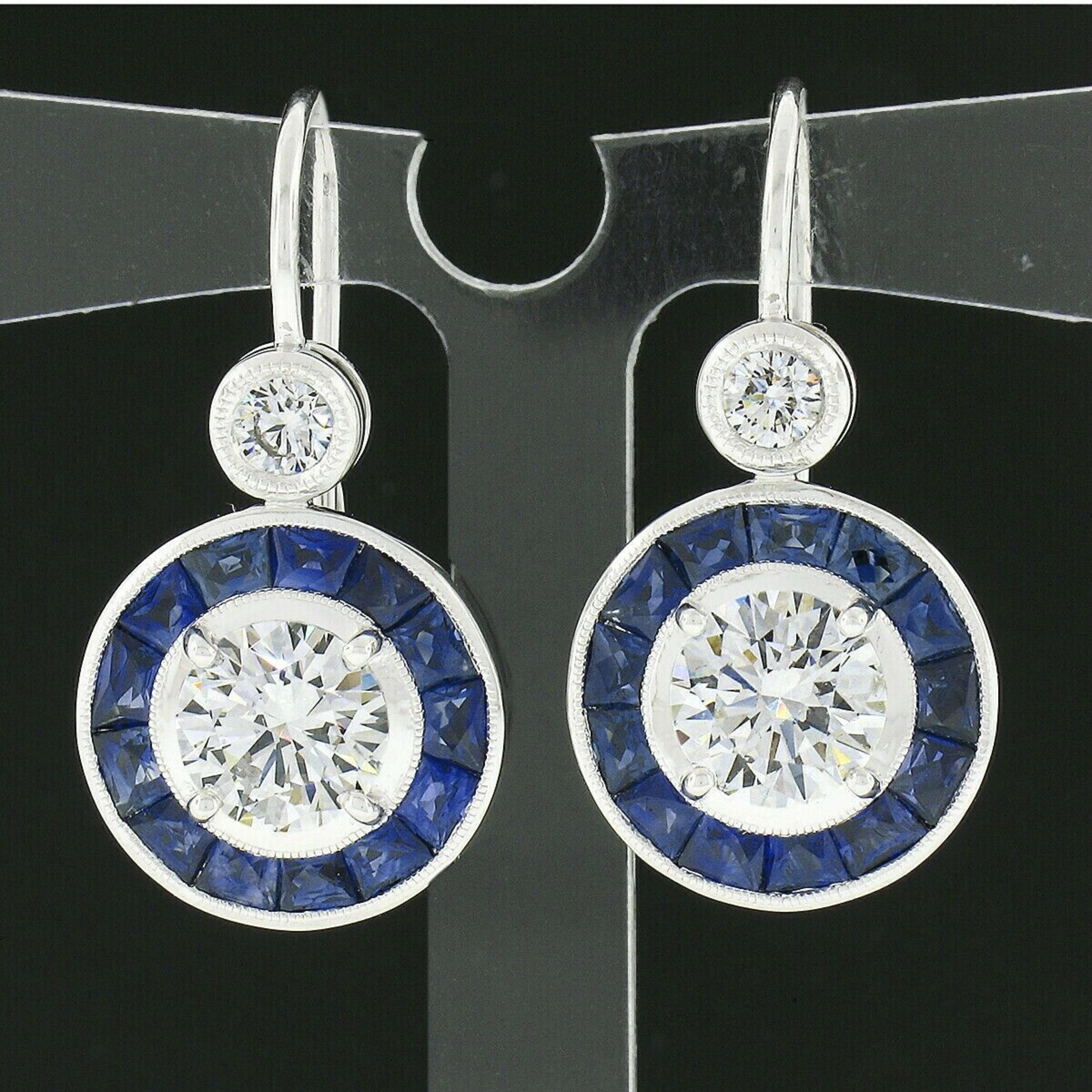 This spectacular and very well made pair of drop earrings is newly crafted in solid 14k white gold and feature two round brilliant cut diamonds that have both been certified by GIA surrounded by a gorgeous halo of natural sapphire stones. The two