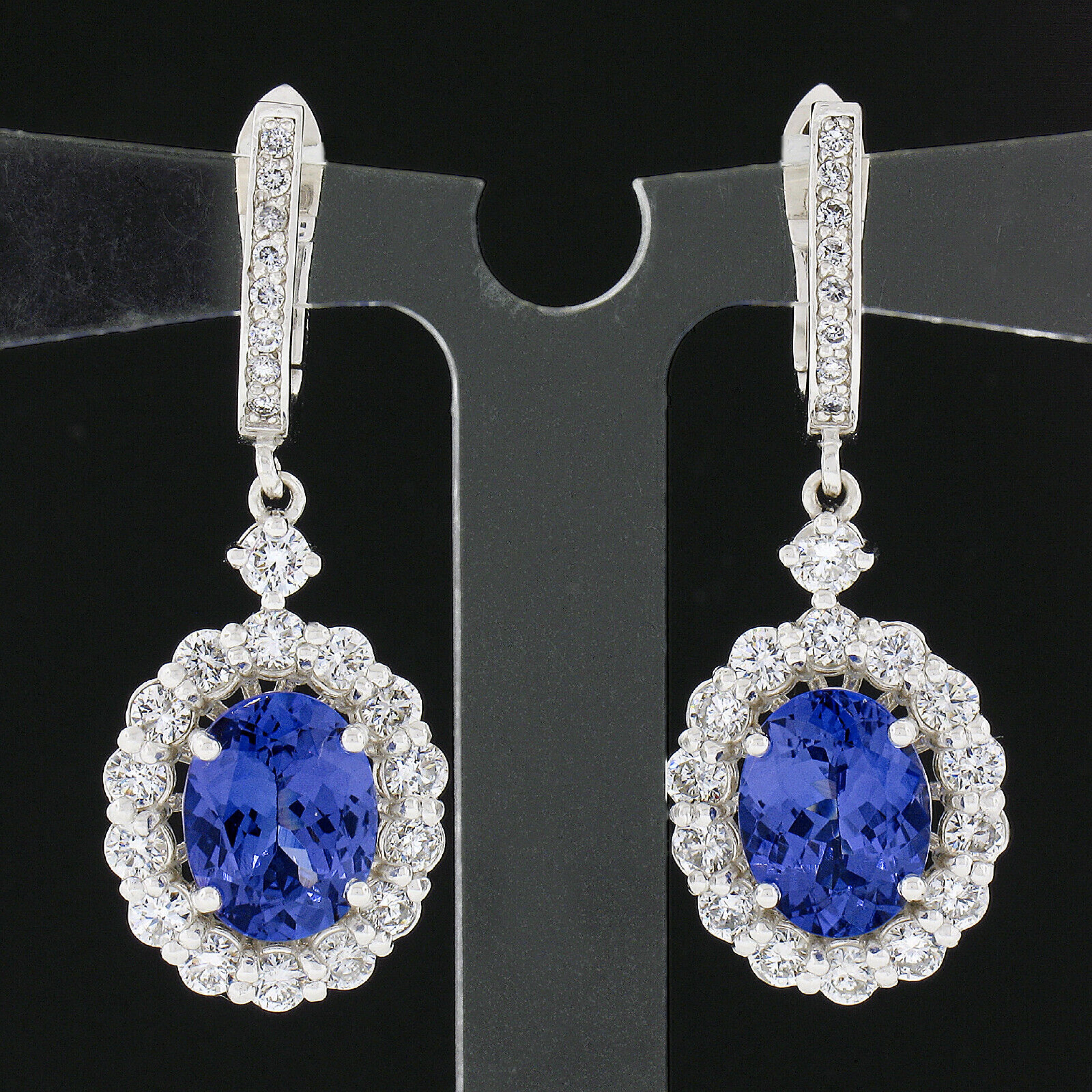 These gorgeous, custom designed, earrings are newly crafted from solid 14k white gold and feature a drop dangle style that carries a stunning tanzanite with fine quality, round brilliant cut, diamonds throughout. The top of the earrings are neatly