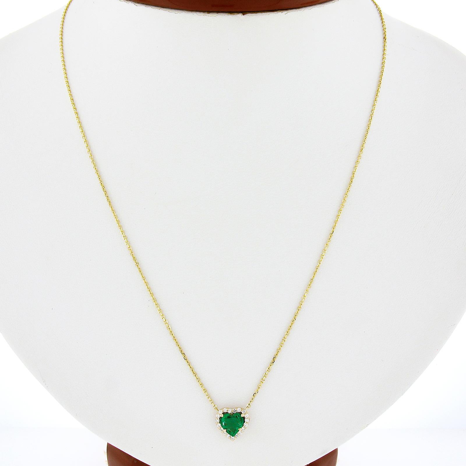 This brand new pendant necklace is crafted in solid 14k yellow gold and features an outstanding emerald gemstone that sits at the center of a brilliant diamond halo. This gorgeous emerald has an exceptional heart brilliant cut with a super