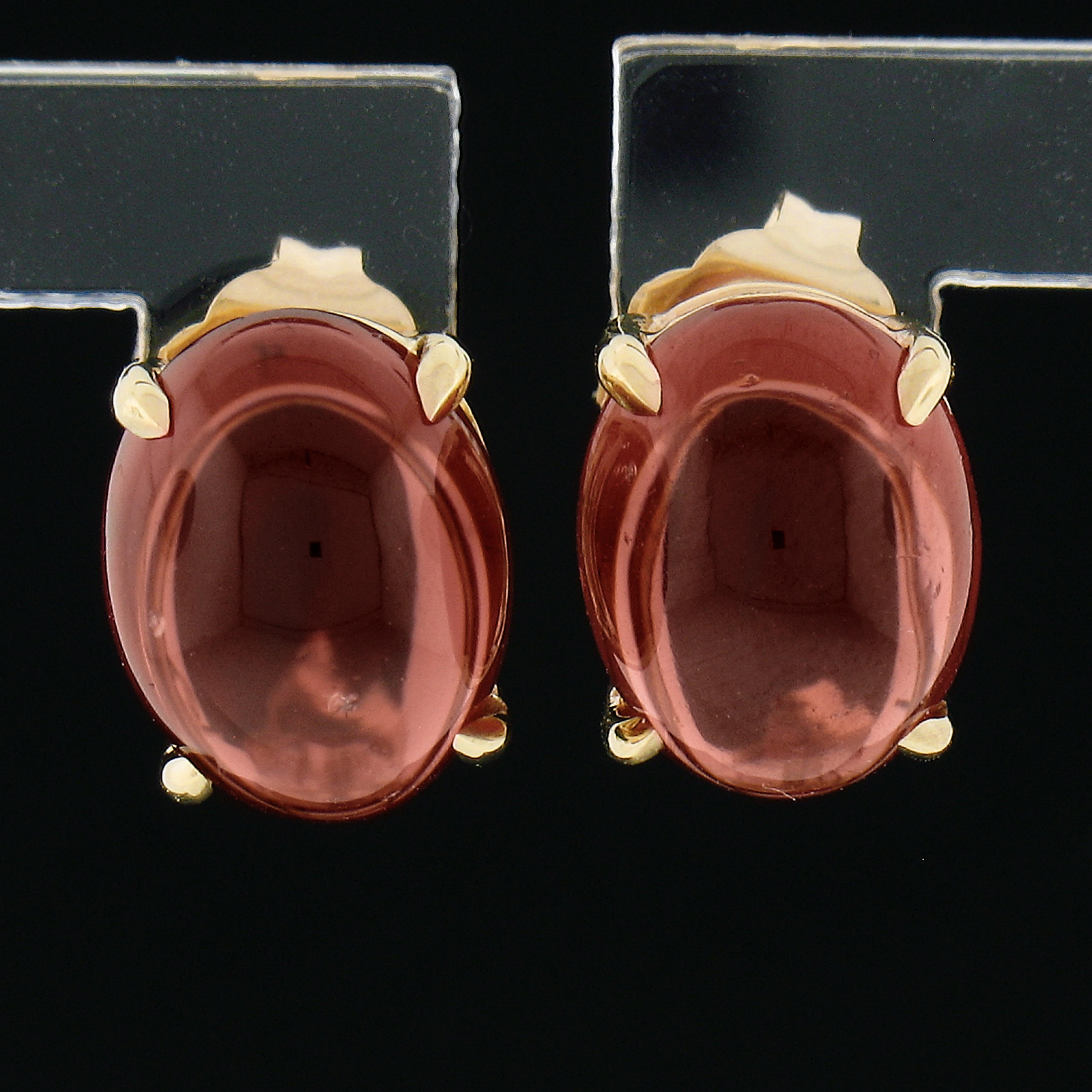 This gorgeous pair of earrings is crafted in solid 14k yellow gold and set with oval cabochon cut natural garnet stones. These beautiful deep brownish red garnets are neatly claw-prong set on open oval baskets studs, and are secure with posts and