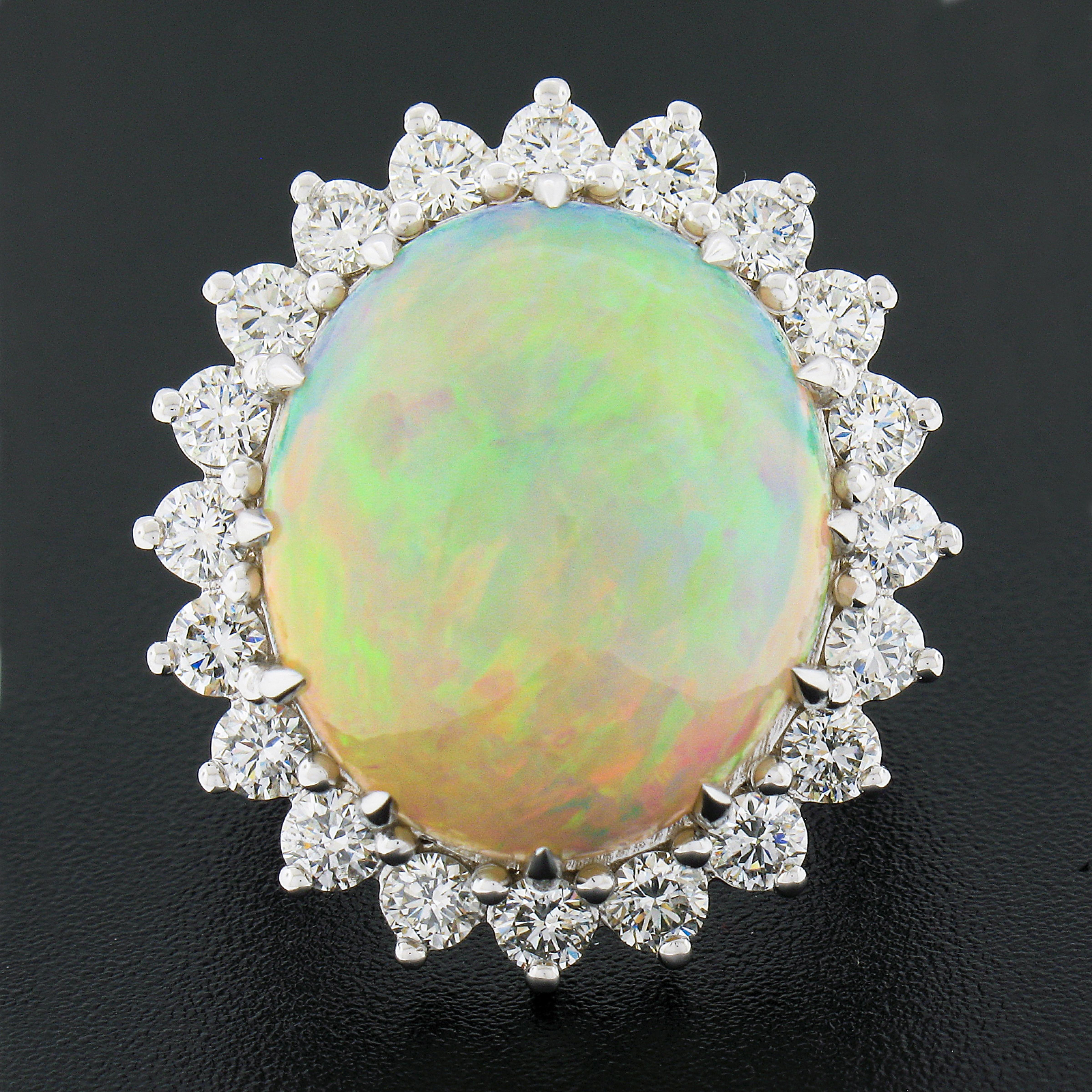 This magnificent, brand new, fancy cocktail ring is crafted in solid 18k white gold and features a large and absolutely breathtaking natural opal gemstone neatly and elegantly multi-prong set at the center of stunning halo design. The 15.47 carat