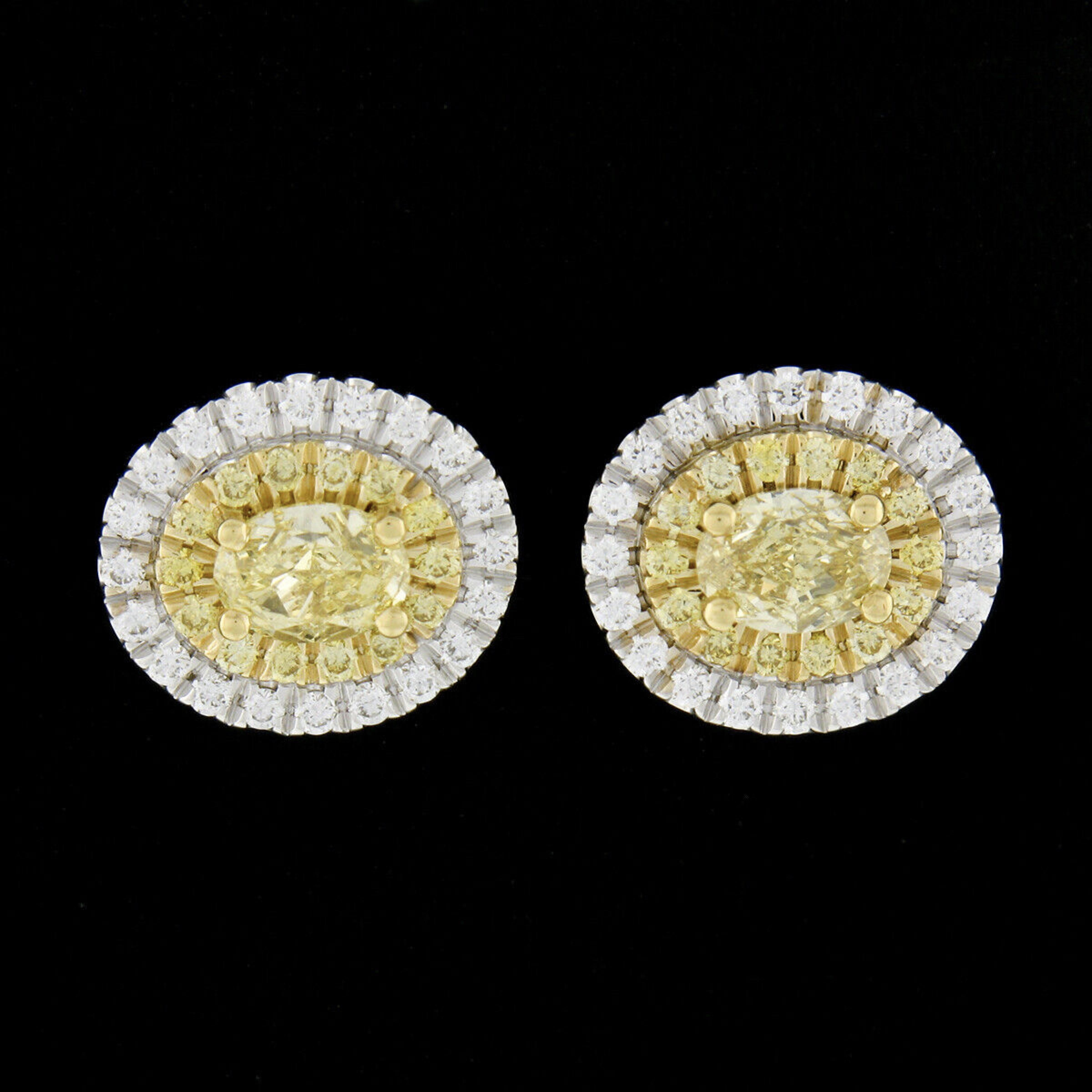 This fiery and lively pair of diamond oval stud earrings is newly crafted in solid 18k white gold and features an oval brilliant cut fancy yellow diamond neatly prong set in 18k yellow gold at the center of a brilliant dual halo design. The two