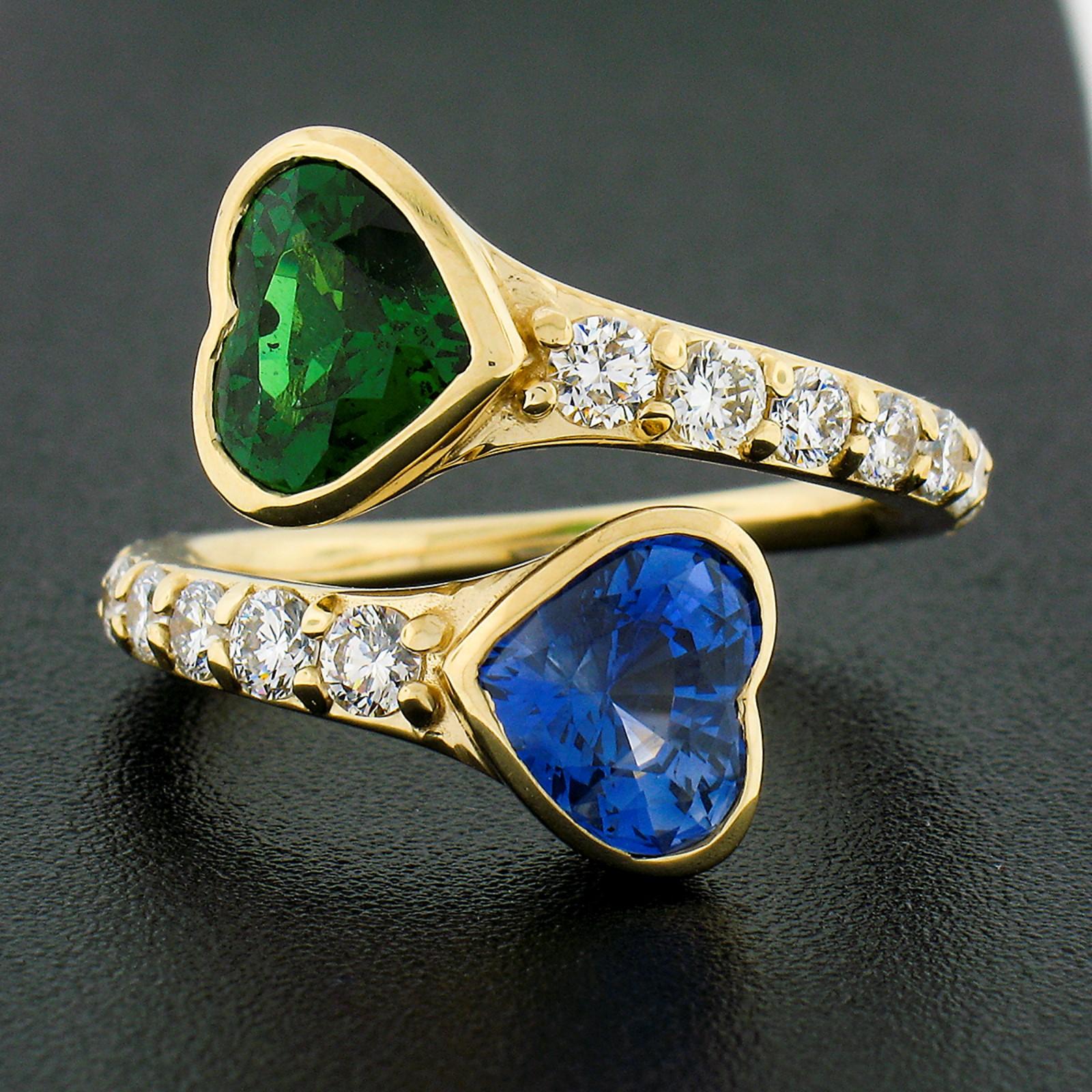 This magnificent and very well made ring is newly crafted in solid 18k yellow gold and features a beautiful bypass design that features a heart brilliant cut sapphire and tsavorite stone, in which both have been certified by GIA. The are both