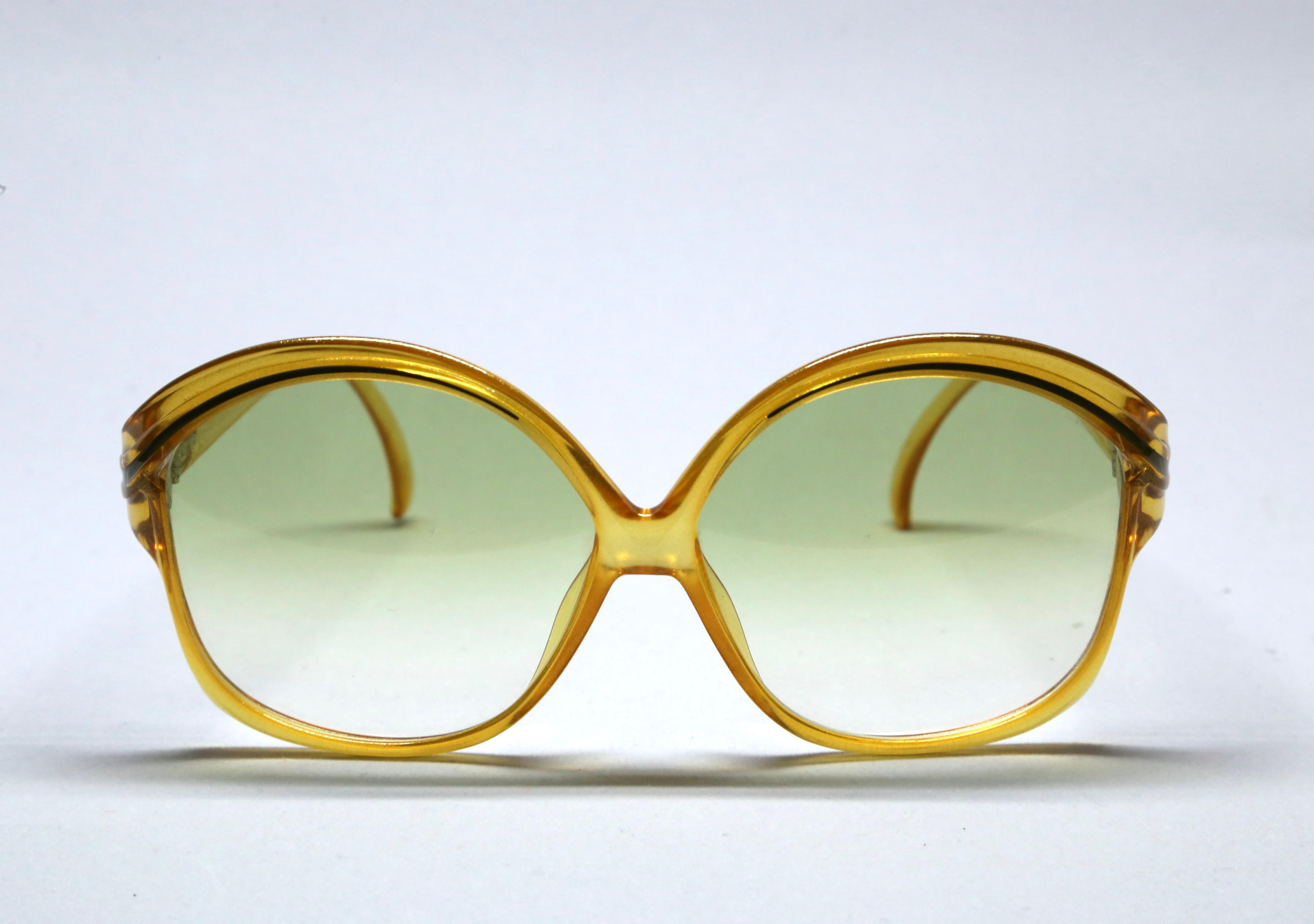 Oversized, transparent amber-yellow acetate sunglasses with black accents and green gradient lenses from Christian Dior dating to the 1970's.  Approximate measurements: Frame width 142 cm and length 64 mm; Arm length 120mm. Made in Germany. New/old
