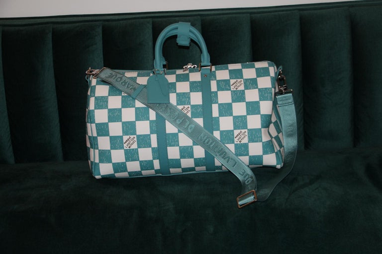 This superb Keepall Bandoulière 45 bag is all made in leather with a Damier checkerboard pattern in turquoise blue and white. Its leather top handles, side bands, and nametag are also in teal. The squares look as if they were drawn and filled in