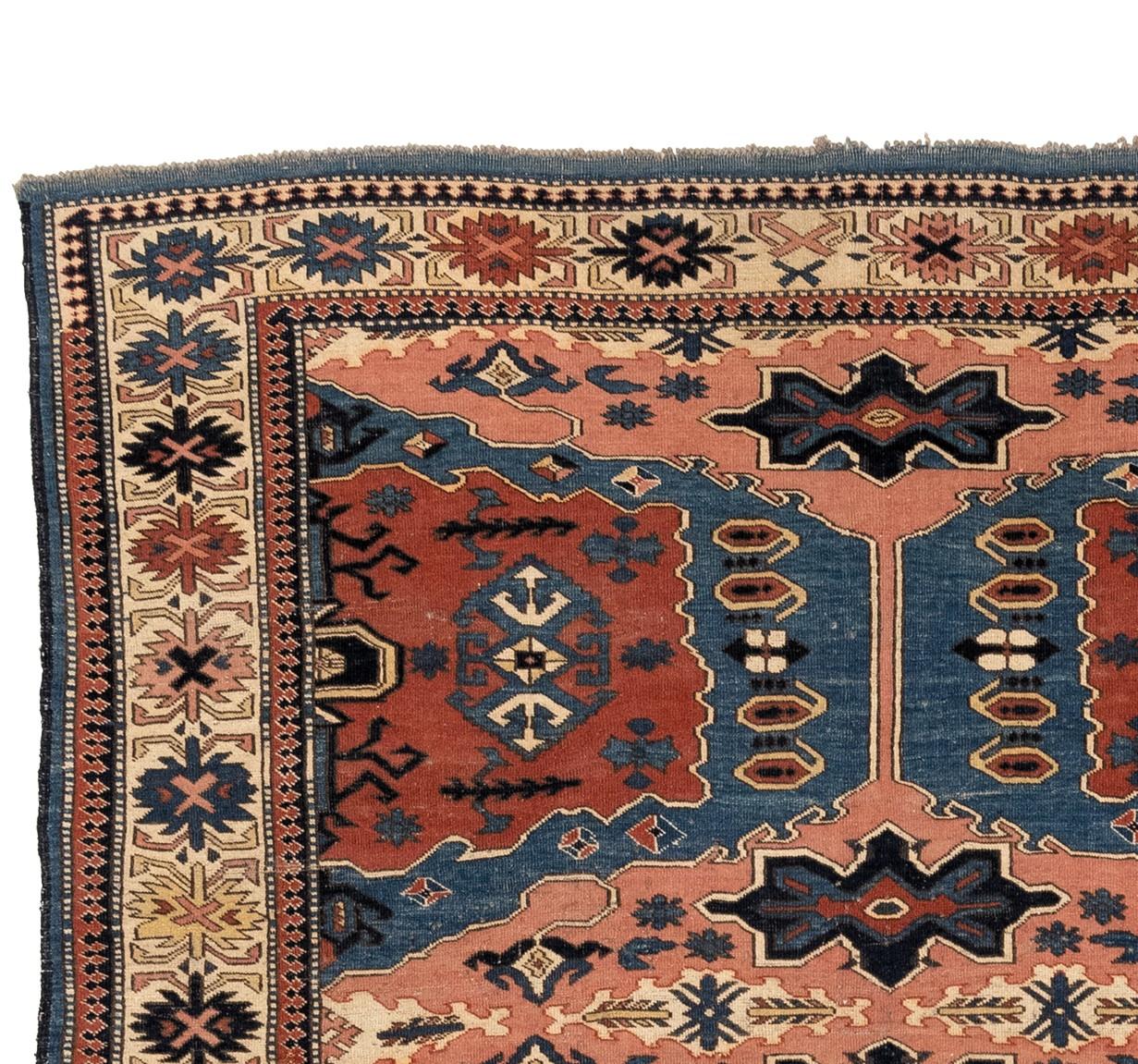 This pinwheel rug is a stunning tribute to the 19th century Kazak pinwheel rugs. Its bold color scheme blends rich blues, peachy tones, and fiery reds with ivory blues, deep navies, and fresh greens to create a mesmerizing display of intricate line