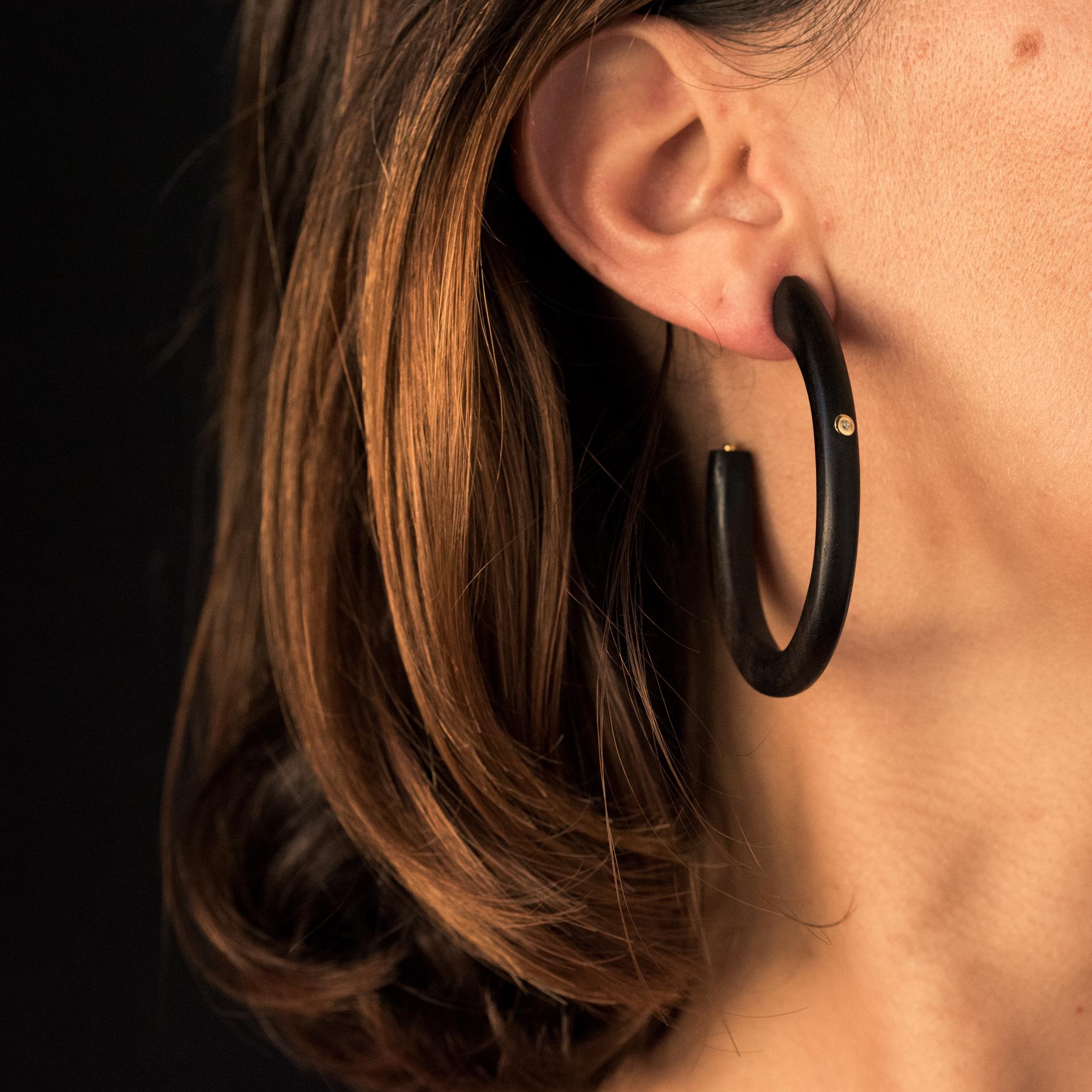 For pierced ears.
Earrings in ebony.
These large earrings are open, oval and cylindrical. Each ebony creole earrings is set on the front of a diamond. The hanging system is a silver butterfly.
Total weight of diamonds: 0.020 carat