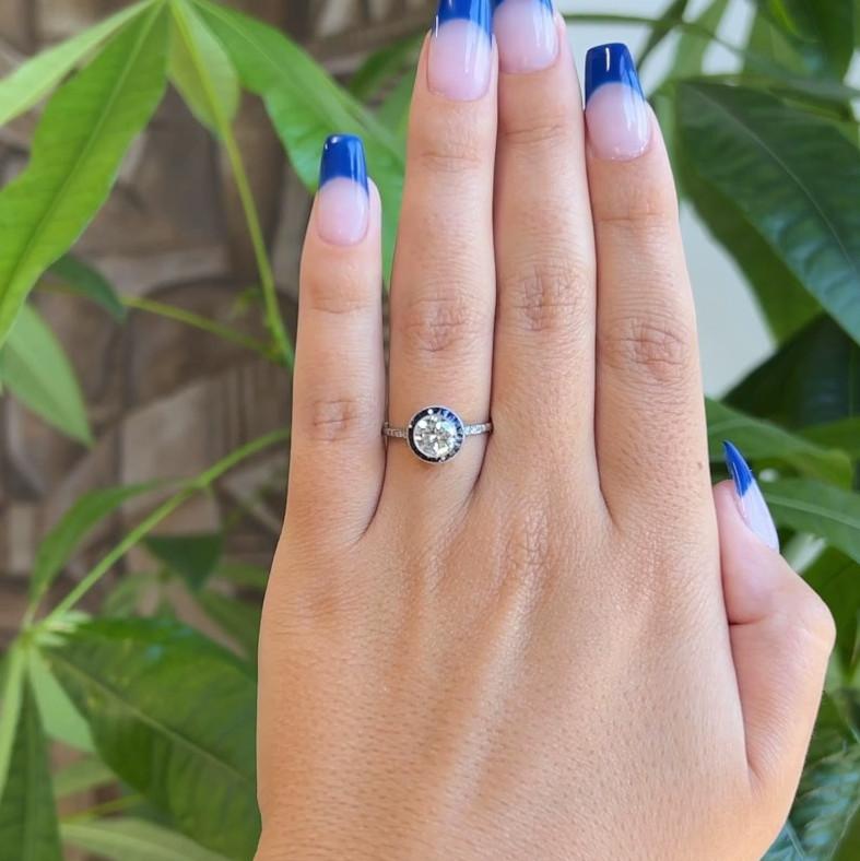 Ein Art Deco inspirierter Diamant Saphir Halo Verlobungsring. Mit einem Diamanten im Übergangsschliff von 0,87 Karat, eingestuft als Farbe I-J, Reinheit I1. Akzentuiert durch 17 Saphire im französischen Schliff mit einem Gesamtgewicht von ca. 1,00