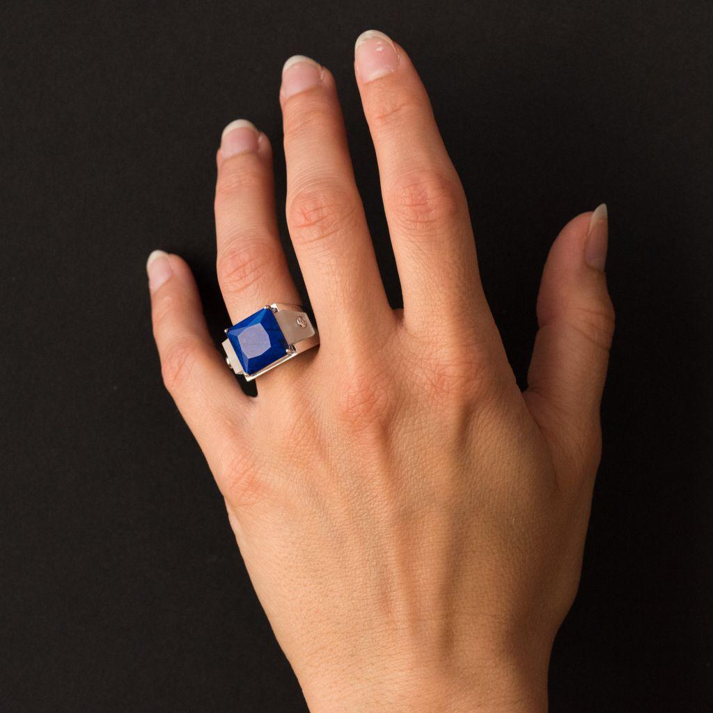 Ring in 18 carats white gold.
White gold ring with geometric lines, it is set on its top with a facetted lapis lazuli shouldered on either side of a rock crystal that follows the contours of the ring and set in the center of a brilliant cut