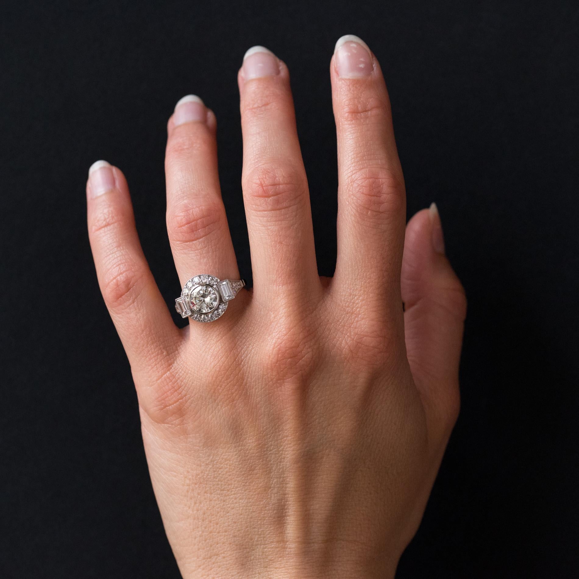 Ring aus Platin.
Prächtiger runder Ring im Art-Deco-Stil, in der Mitte mit einem Brillanten besetzt, der auf beiden Seiten von 2 Baguette-Diamanten mit Millegrains und 2 x 5 Brillanten auf den Rundungen getragen wird. Auf beiden Seiten des Kopfes am