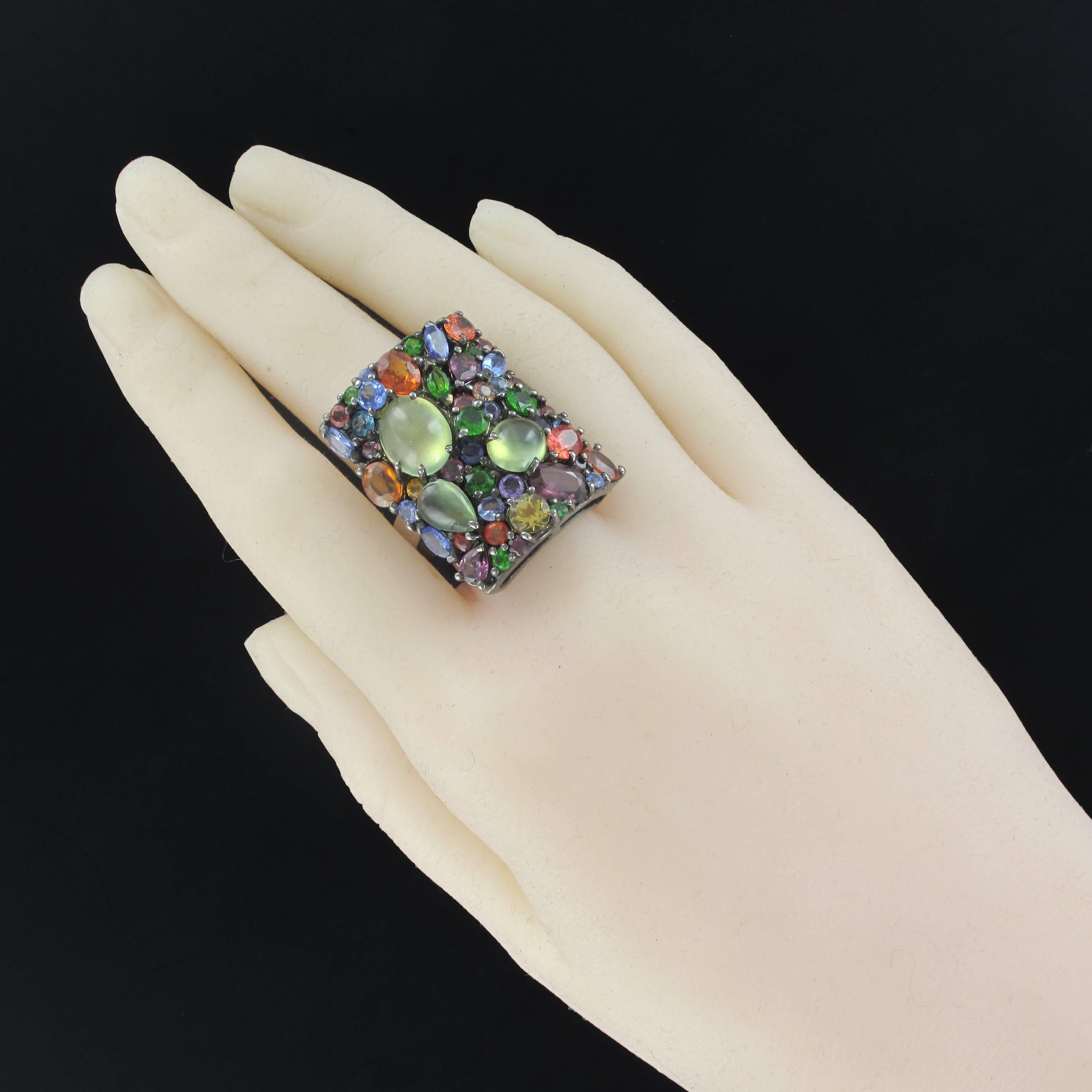 Ring in Silver, 925.
Rectangular shape; this imposing ring is set with claws of a multitude of precious stones with different shapes and sizes: prehnites, tanzanites, rhodolite, orange garnets, sapphires, diopsides and topazes. The tray is curved to