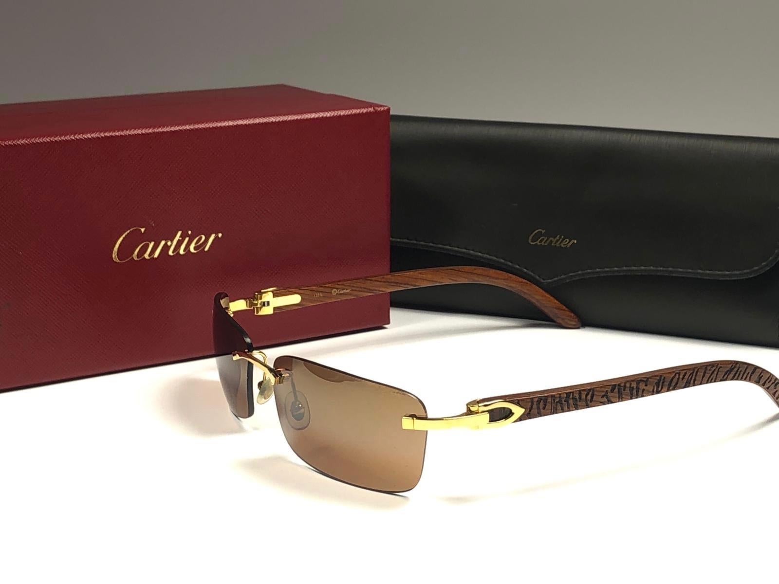 New Original Cartier Sunglasses with carved wood temples and honey brown spotless uv protection lenses.  
Frame with the front and sides in gold.  
All hallmarks.  Gold Cartier signs on the ear paddles. 
Both arms sport the c from Cartier on the