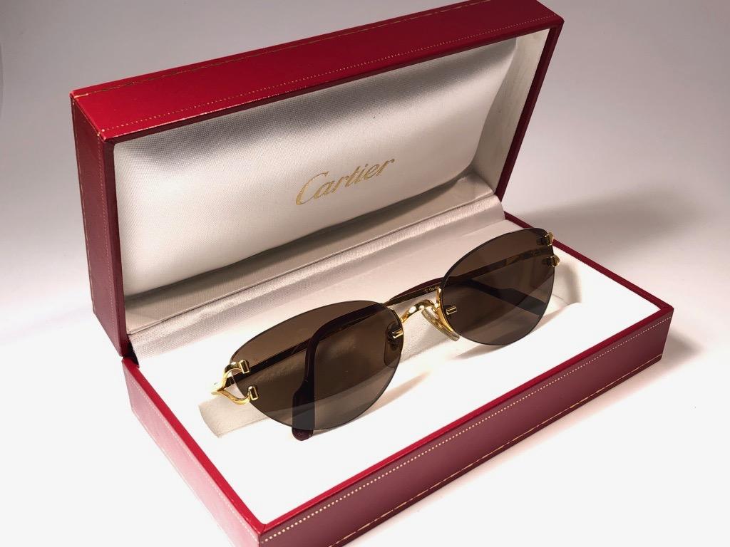 New Cartier Condotti unique rimless sunglasses with brown (uv protection) lenses. Frame with the front and sides in gold. All hallmarks. Cartier gold signs on the black ear paddles. These are like a pair of jewels on your nose. Beautiful design and