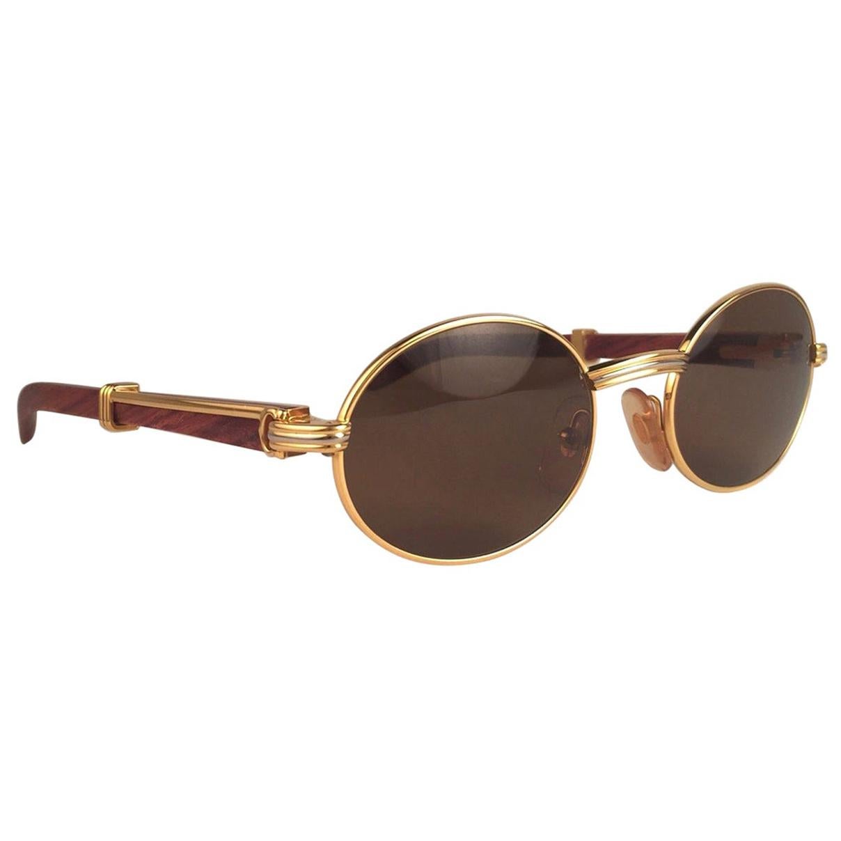 Nouveau Original Rare Lunettes de soleil Cartier classy Giverny 1992 en or jaune et blanc avec branches en bois de rose et verres anti-UV sans taches en brun miel.  
Cadre avec le devant et les côtés en or jaune.  
Tous les poinçons.  Signes Cartier