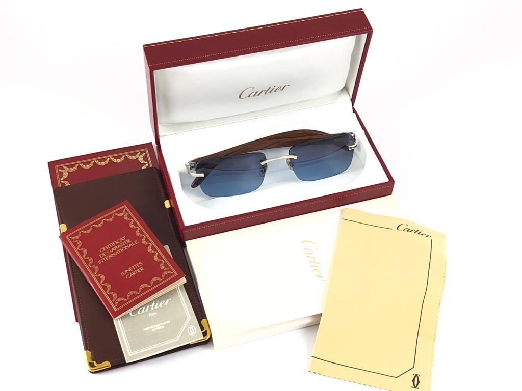 Vintage Original Cartier Sunglasses with wood temples and blue gradient uv protection lenses.  
Frame with the front and sides in platine.  
All hallmarks. Cartier signs on the ear paddles. 
Both arms sport the c from Cartier on the temple.  These