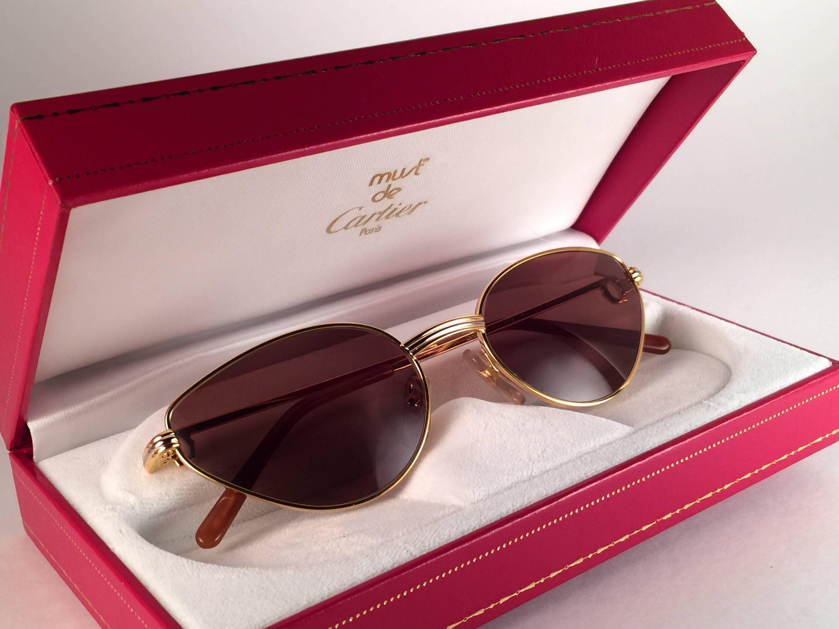 Neu 1988 Cartier Rivoli Vendome Cat Eye Sonnenbrille mit neuen Honig braun  (UV-Schutz) Linsen.  Die Katzenaugenfassung ist auf der Vorderseite und an den Seiten in Gelb- und Weißgold gehalten.  Alle Markenzeichen. Rote Emaille-Ohrstöpsel. Beide