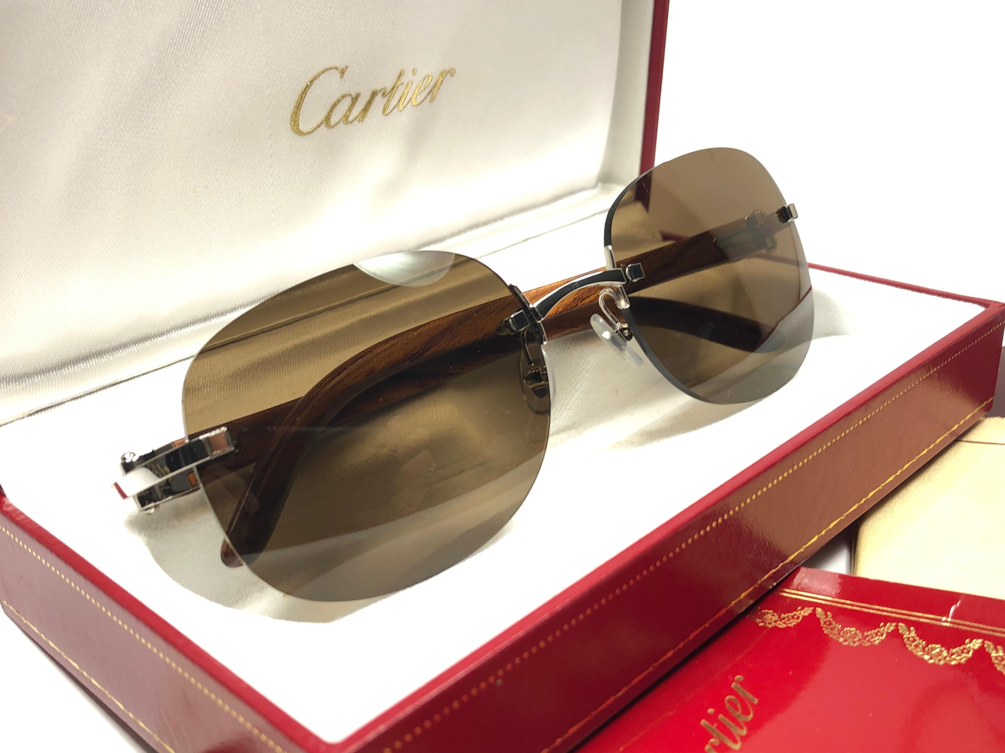 New Original Rare White gold plated Cartier Sunglasses with rosewood temples and honey brown spotless uv protection lenses.  
Frame with the front and sides in white gold.  
All hallmarks.  Gold Cartier signs on the ear paddles. 
Both arms sport the