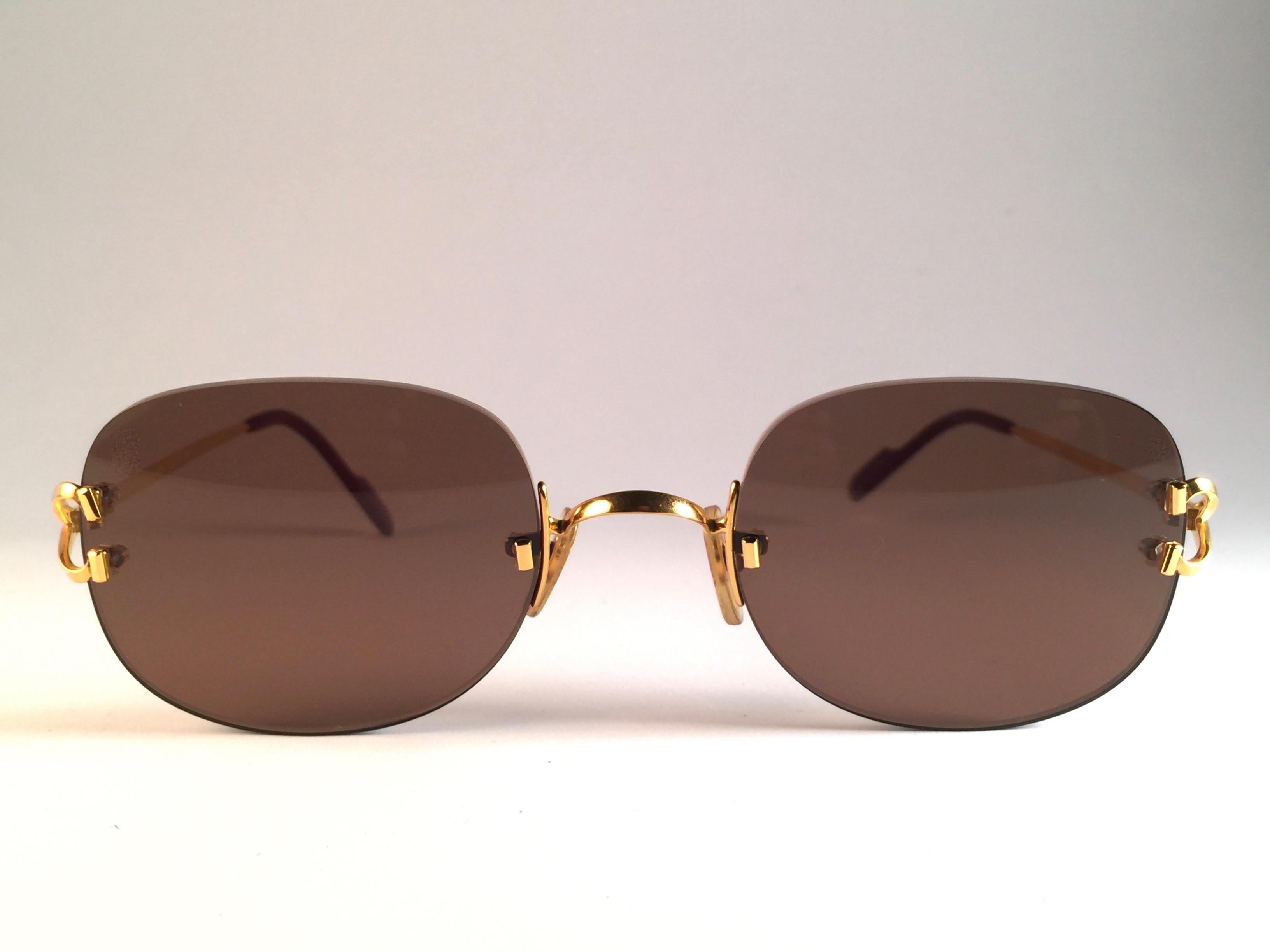 Nouvelles lunettes de soleil sans monture Cartier Serrano uniques avec des verres bruns (protection contre les UV). Cadre dont le recto et les côtés sont dorés. Tous les poinçons. Signes en or de Cartier sur les palettes d'oreille noires. Ils sont