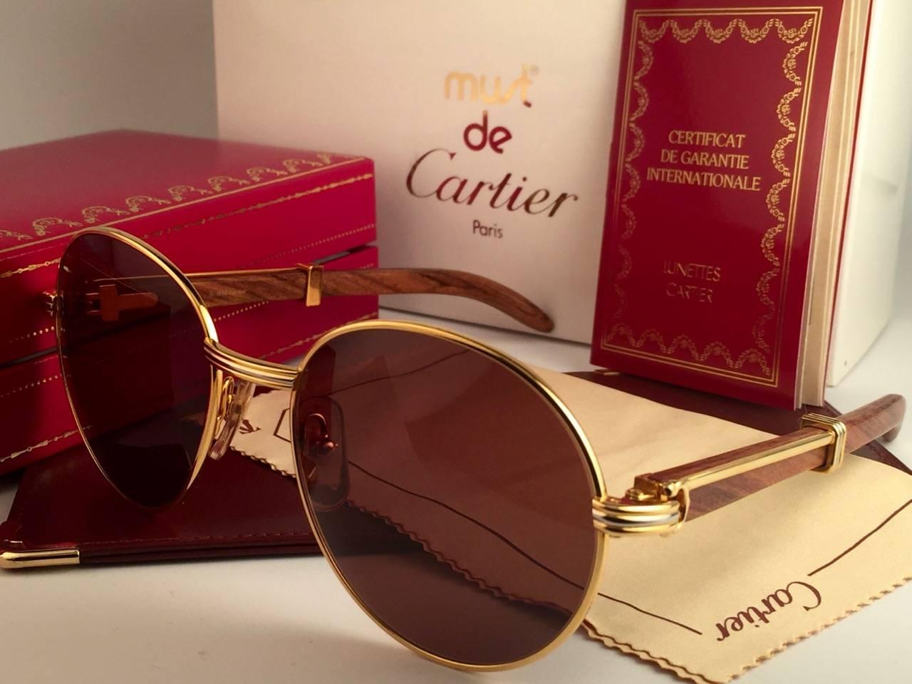 Nouvelles lunettes de soleil originales 1990 Cartier Bagatelle Wood de la très convoitée série Precious Wood avec branches en bois et verres marron miel (protection contre les UV). 
Le cadre présente une face et des côtés en or jaune et en or blanc.