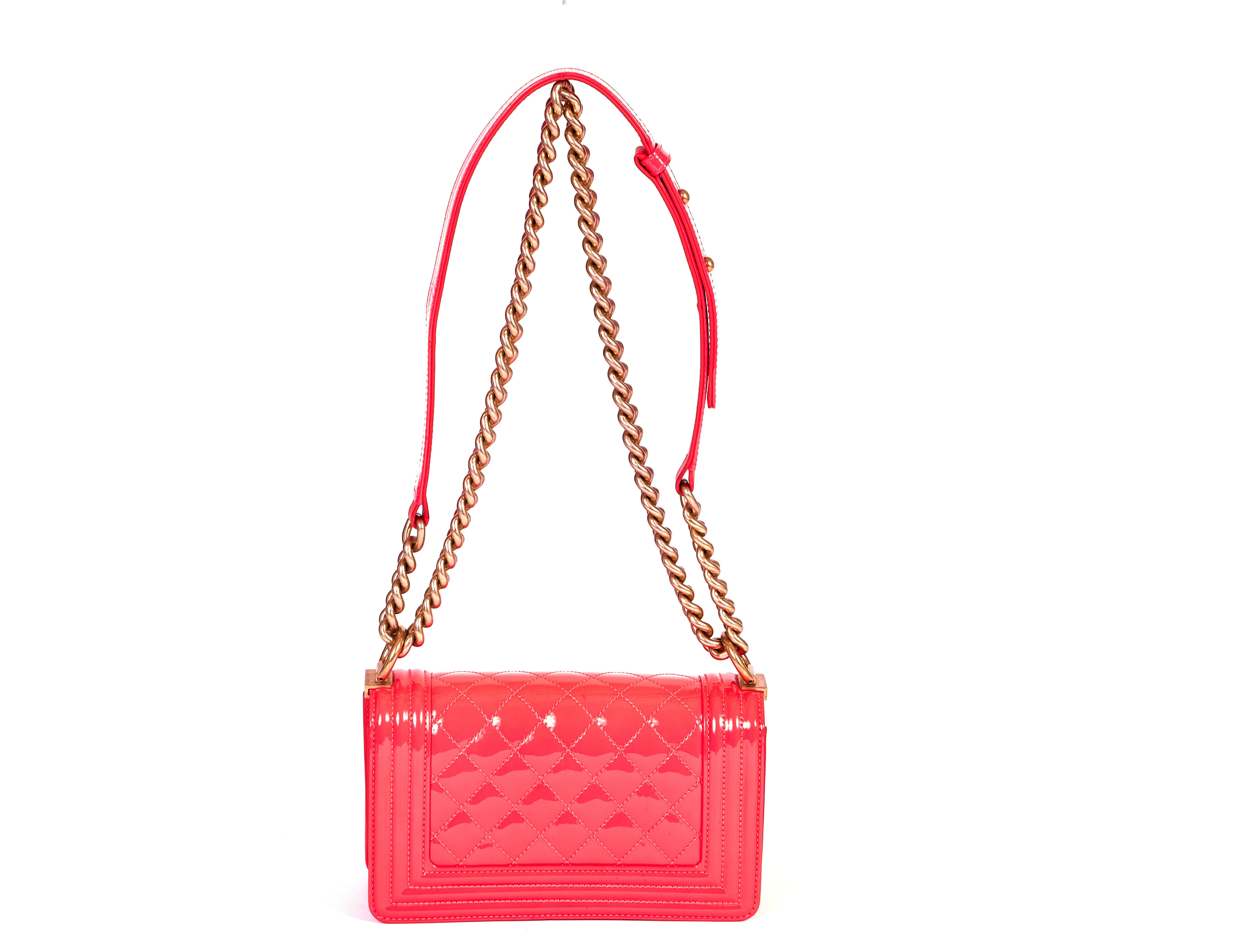 This glossy patent neon pink Chanel Boy Bag comes with a big chain in gold, which can be worn over the shoulder or cross body. Partial plastic still on hardware. The shoulder drop is 21 inches. It has the original Chanel dust bag. According to the