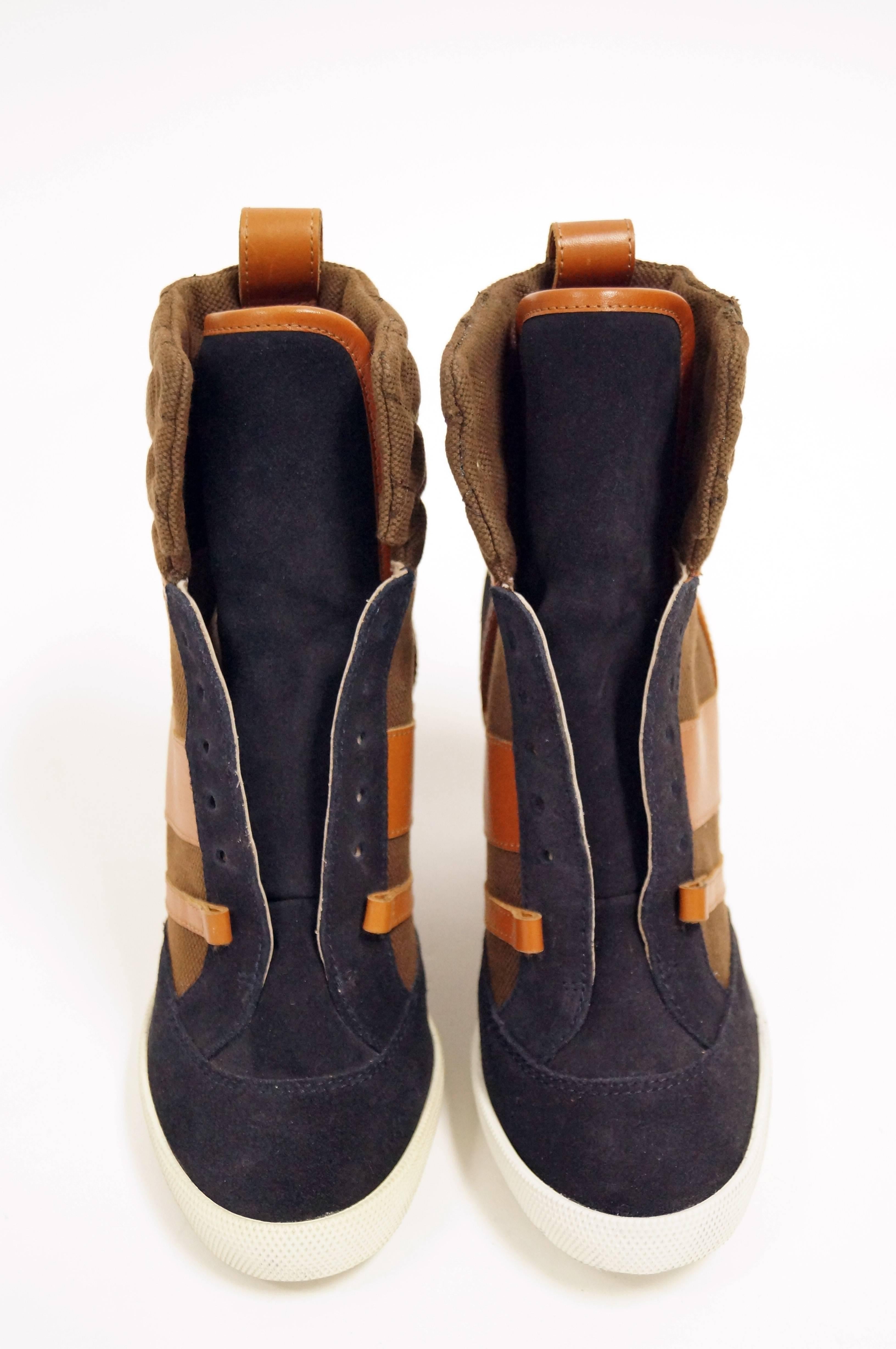 Contemporary wedge sneakers shoes by Chloe in complementary navy blue and orange. The sneakers feature a high collar and tongue, with laces reaching from the toe to the ankle. Wedge, heel, toe, and tongue are covered in navy blue suede. Ankle and