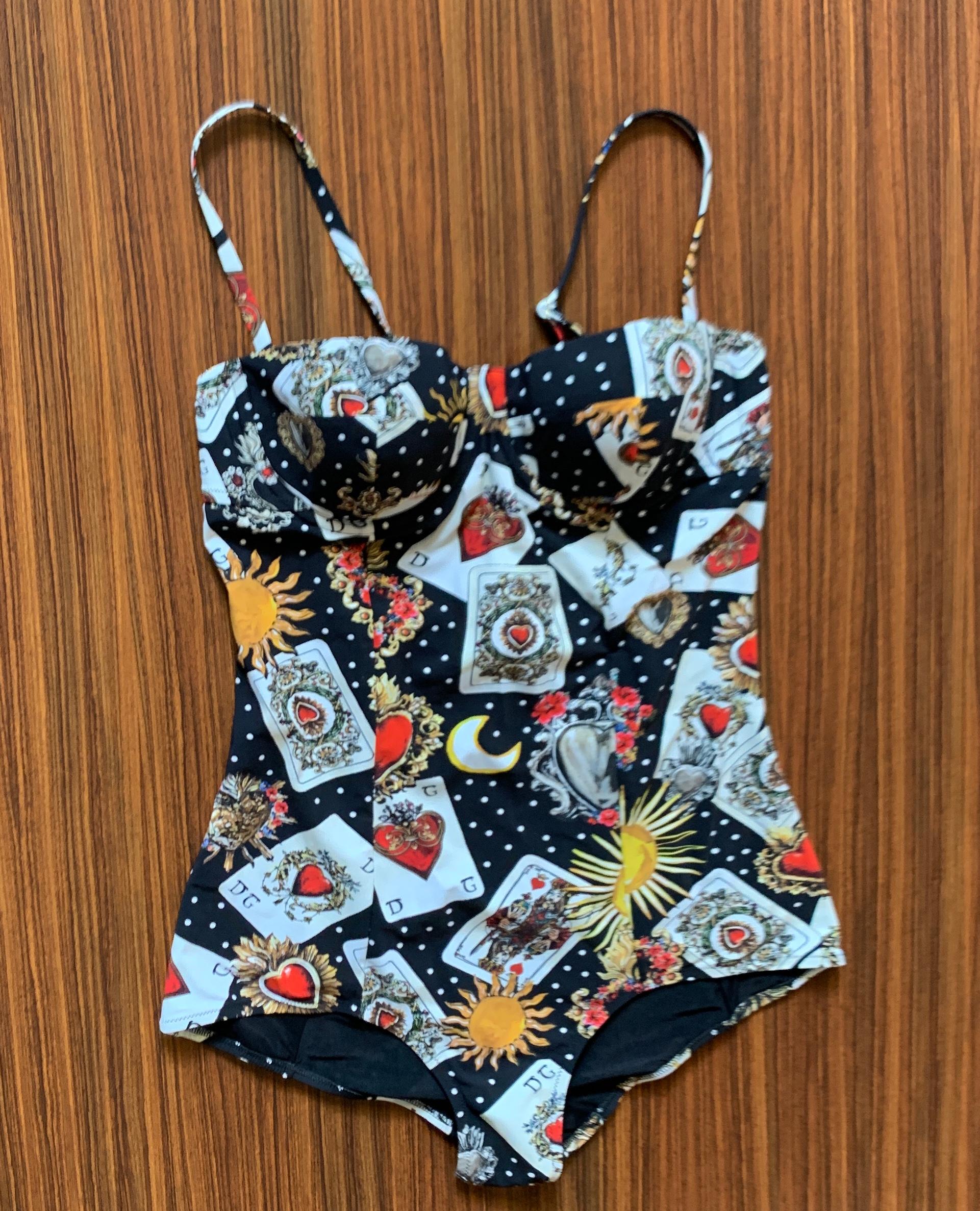 Dolce & Gabbana one-piece swimming suit in black playing card print. Design features distressed DG print cards, sacred hearts, suns, moons, and polkadots throughout. Balconette top has padded cup and underwire. Removable straps, can be worn with