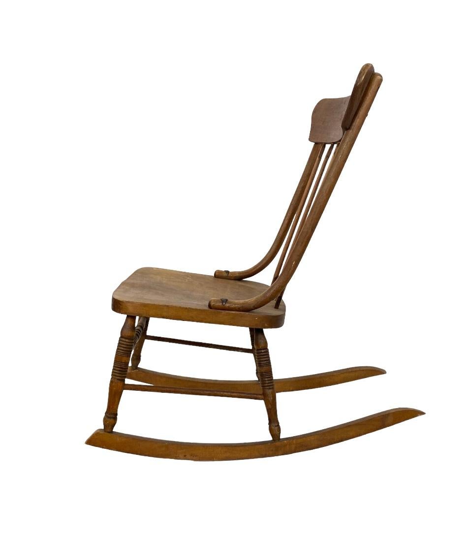 Antique rocking chair constructed of solid wood. High headrest and spindle back with long elegant runner. Of New England origin. Early 20th century. Perfect for the corner next to the fireplace of a country escape. In good condition with age
