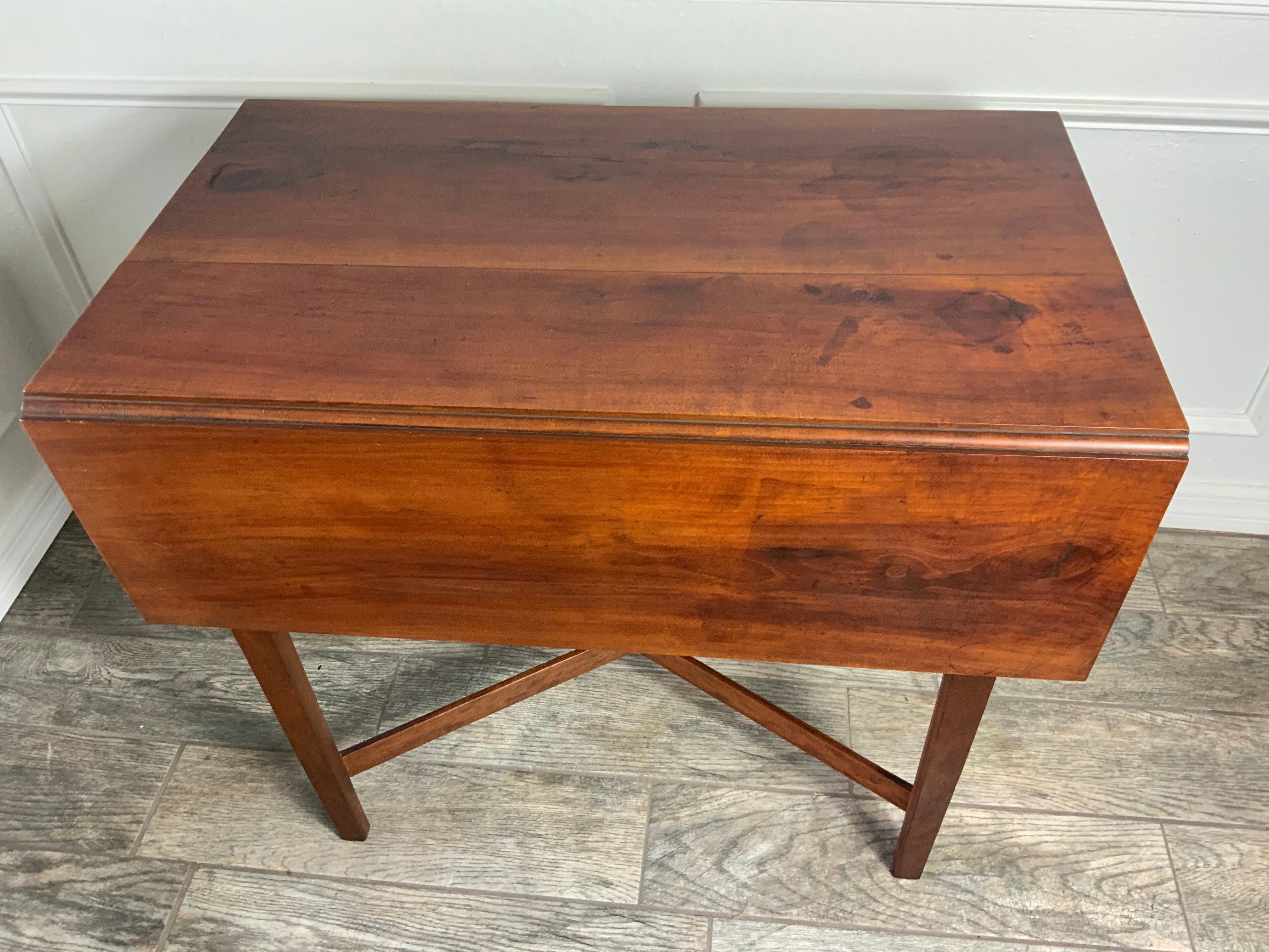A nice early 19th century New England Cherry Pembroke table with a cross stretcher support on tapered chamfered legs.  White Pine secondary case wood with Oak leaf supports. Old refinished surface with a nice color and patina. Hardware and hinges