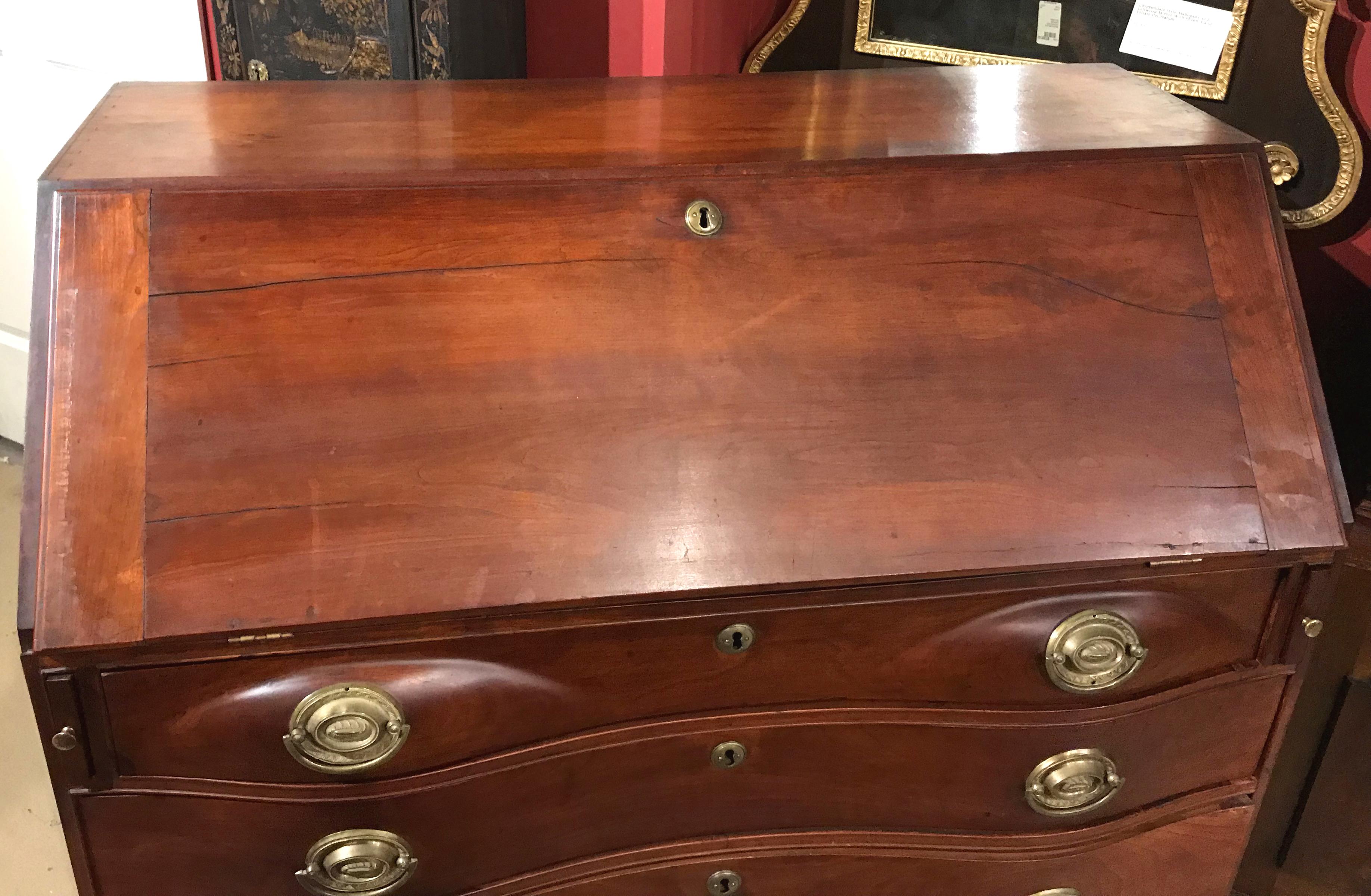 A fine Chippendale cherry oxbow slant front desk with compartmentalized interior over four conforming graduated drawers with replaced oval period brasses, all supported by four nicely carved bracket feet. New England in origin, dating to the late