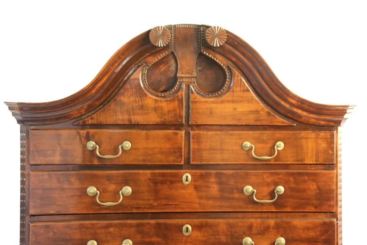 This very unique figured maple chest-on-chest is comprised of two parts. The upper case has enclosed bonnet top with rosettes. The face of the tympanum posseses tear drop cut-outs adorned with chip-carved border along with applied plaques. The top