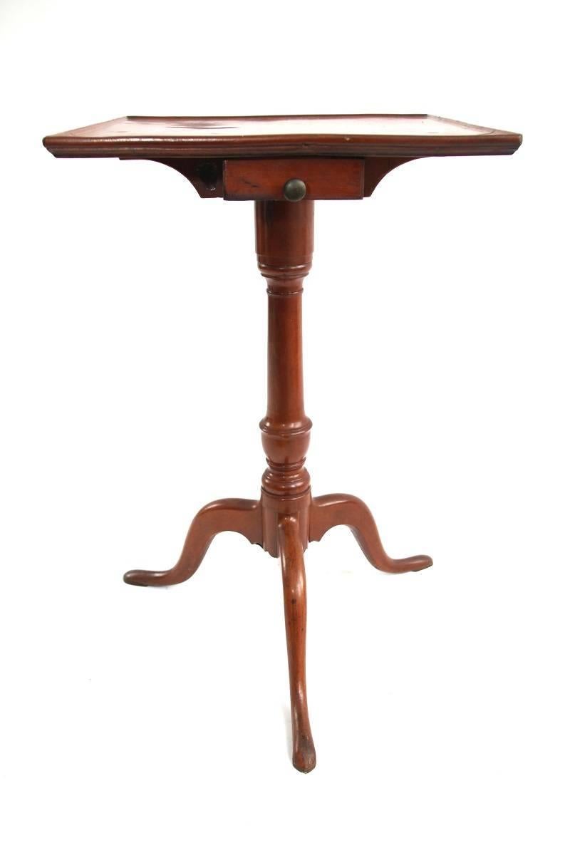 Federal carved cherry candlestand, the square top with an applied beaded edge above a conformingly shaped double-ended candle drawer center-mounted in a molded support on a vase and ring-turned support and tripod cabriole leg base.
 
Probably