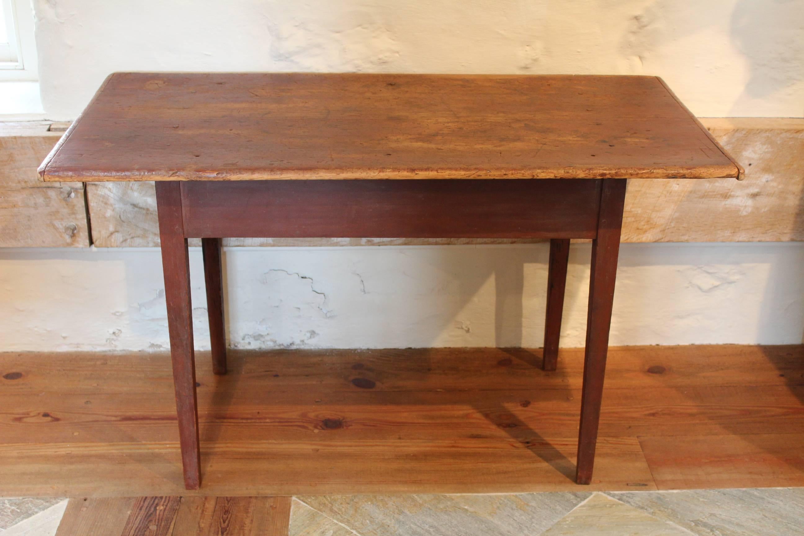 A New England cherrywood and pine tavern table retaining its original red-painted finish. This table features a single board top with bread board ends over tapered legs with pegged construction throughout. 

Measures: H. 28 3/4
