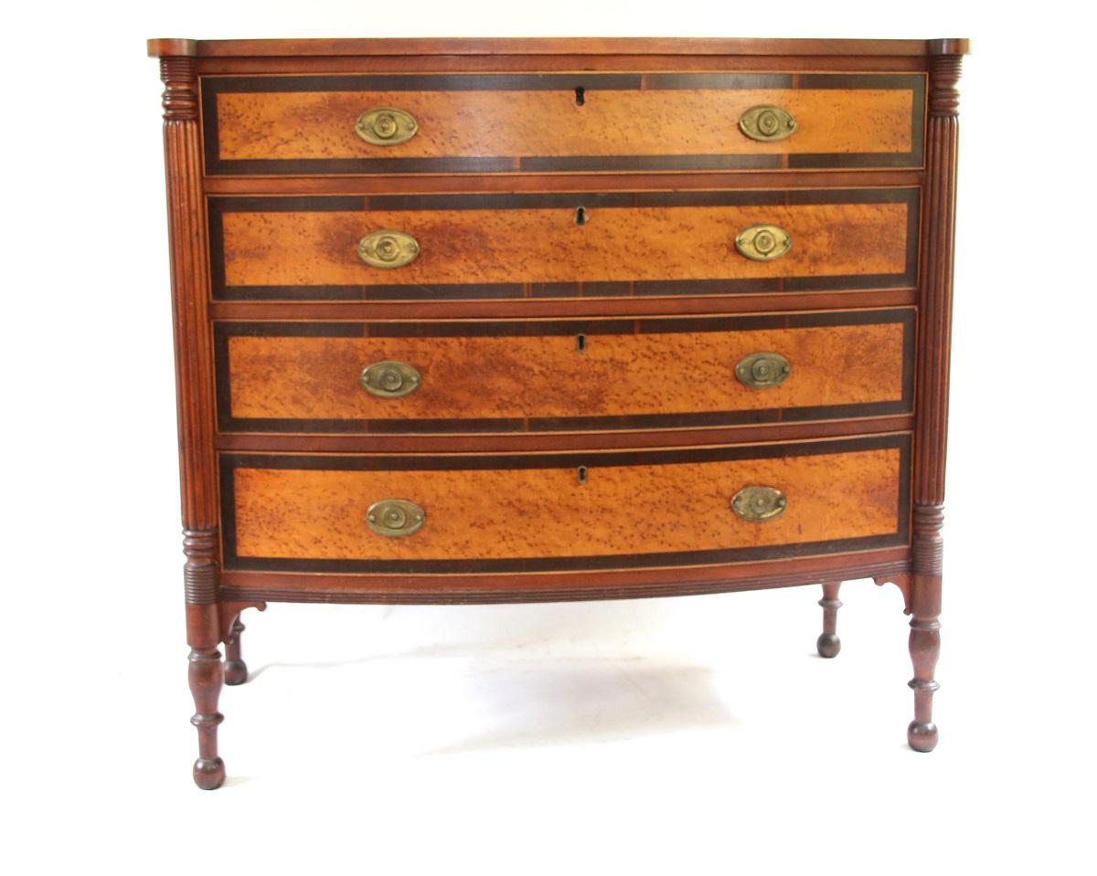 New England Sheraton birch and bird's-eye maple bow front chest of drawers. Rectangular case with bow front and turret corners above a conforming case fitted with four long drawers, each inlaid with bird's-eye maple panels within rosewood banded