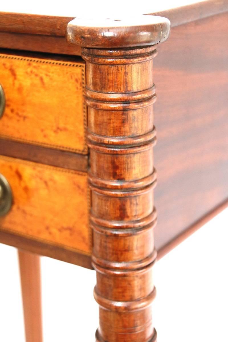 Two-drawer work table possesses a thin mahogany top with bold cookie corners. The legs have a ring-turned upper portion, having reeded shafts with tapering legs. Both drawers are faced with bird’s eye maple beautifully framed with barber pole