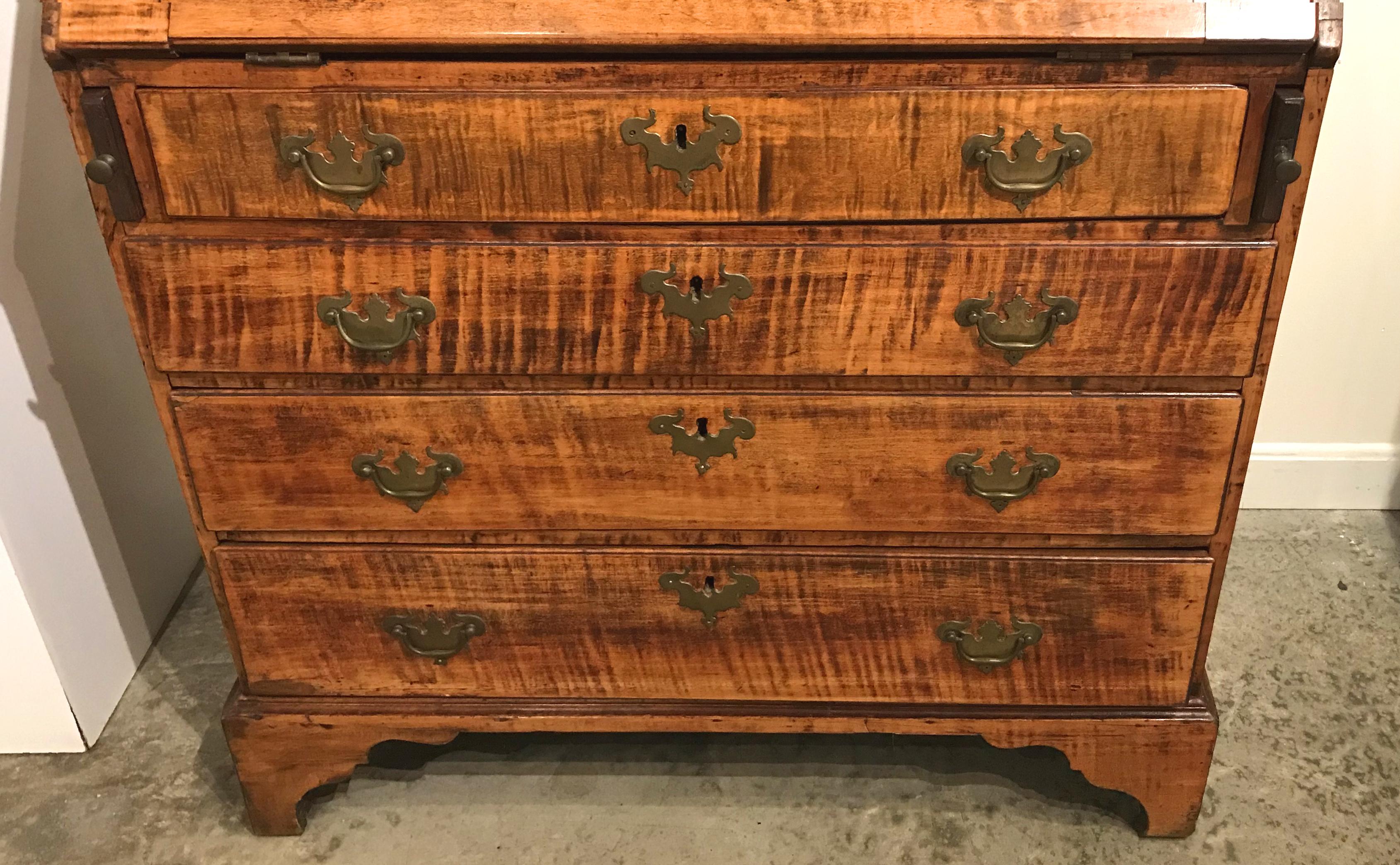 A fine example of a New England tiger maple slant front desk circa 1760 with compartmentalized interior featuring eight valanced open cubbies flanking a central prospect drawer over seven fitted drawers. The lower half of the desk features four