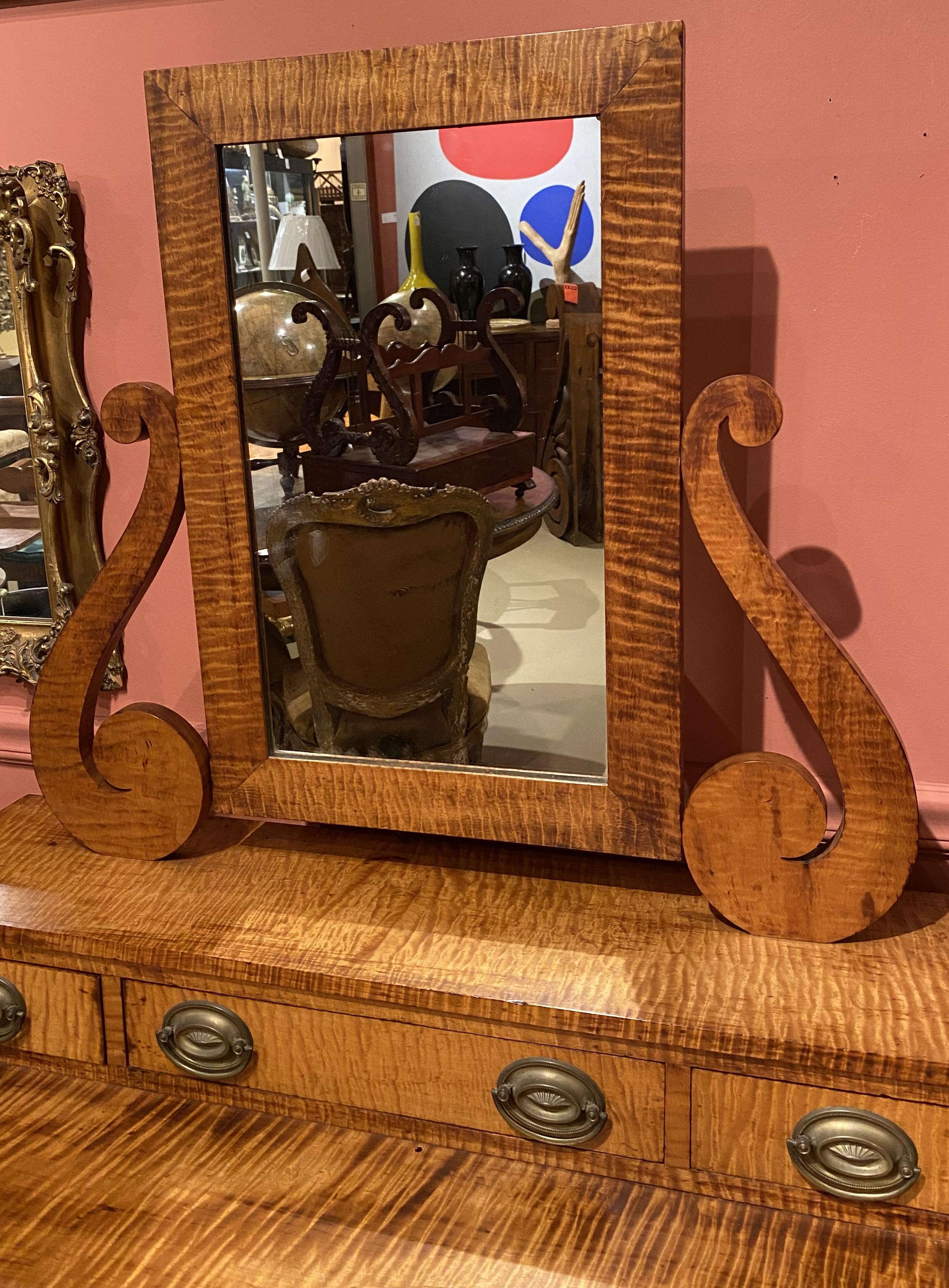 A fine form tiger maple dressing chest with mirror supported by decorative carved scrolls, over three fitted drawers in its upper case, over two long drawers below, each with oval brasses, supported by four turned legs and a rectangular base