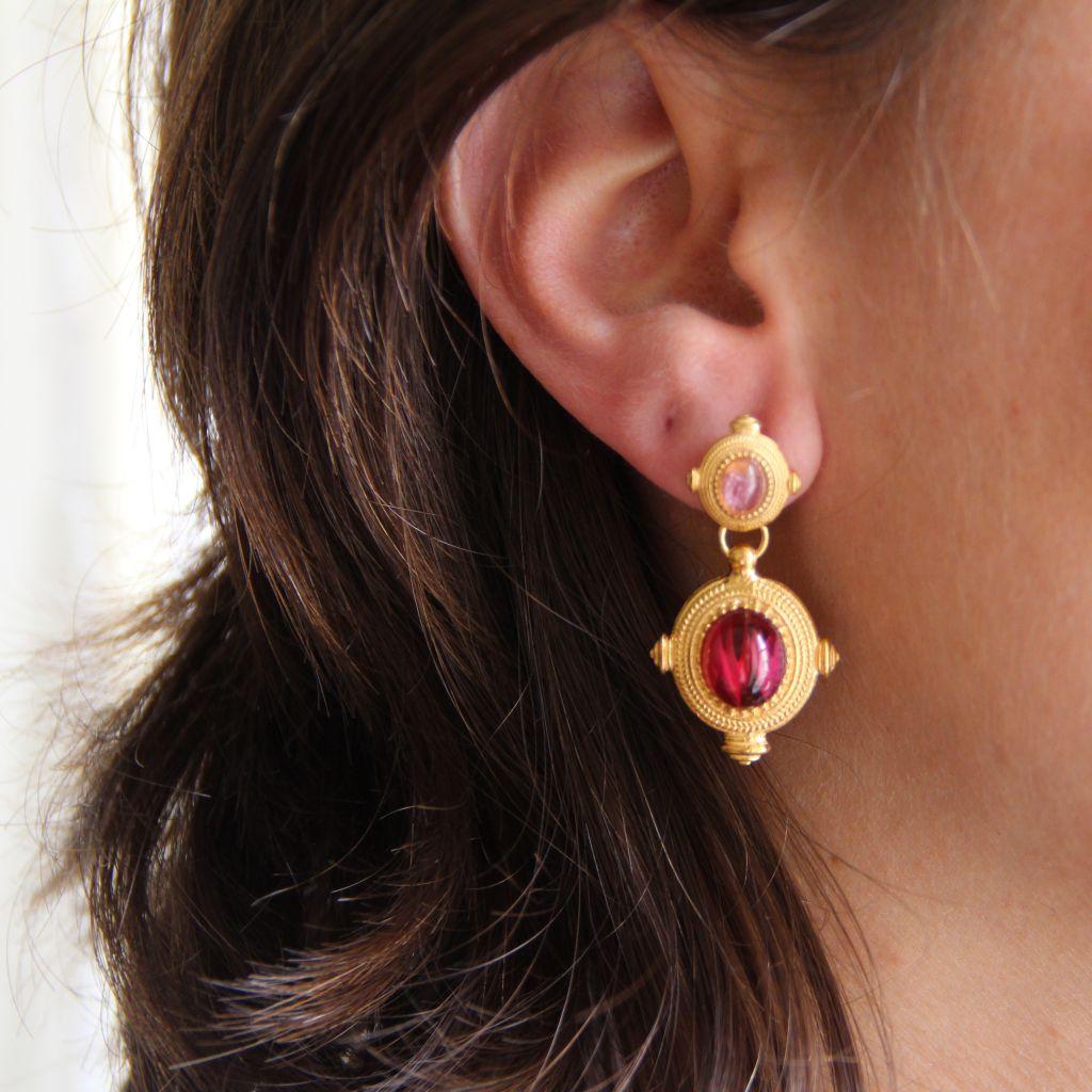 For pierced ears.
Earrings in vermeil, silver covered with yellow gold.
Two oval motifs, one below the other, are set with a pink crystal cabochon above and red cabochon on the bottom motif, surrounded by a chiseled decoration and bordered by a