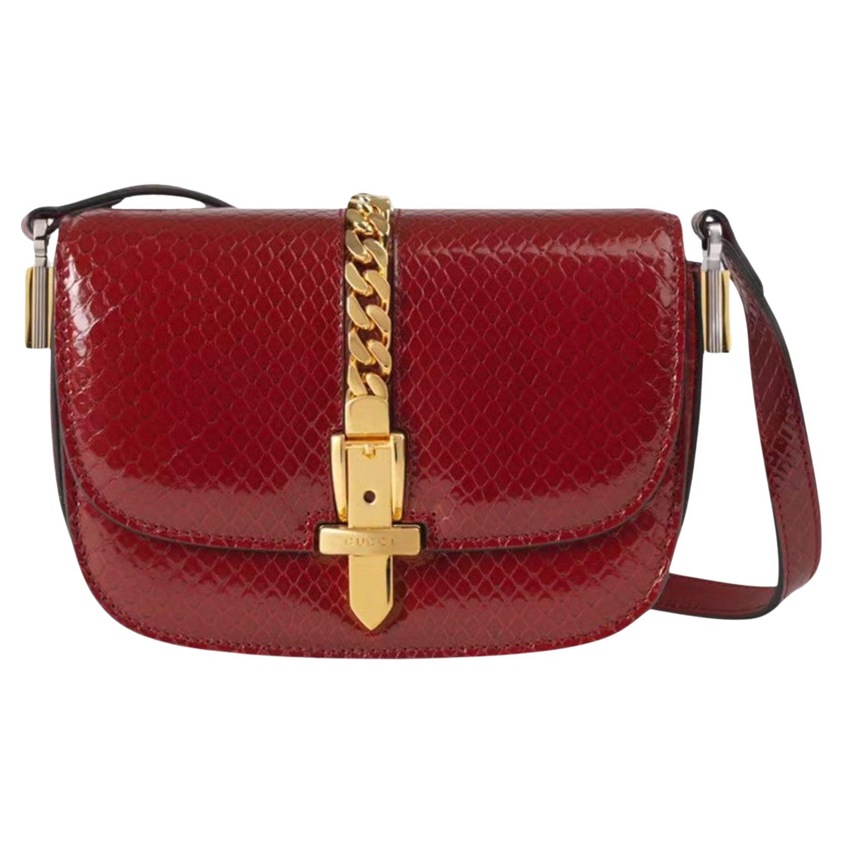The small shoulder bag in burgundy python skin is defined by a narrow gold-toned metal chain fitted to the flap. The softly rounded silhouette is completed with a special mechanism that adjusts the length of the shoulder strap so it can be carried