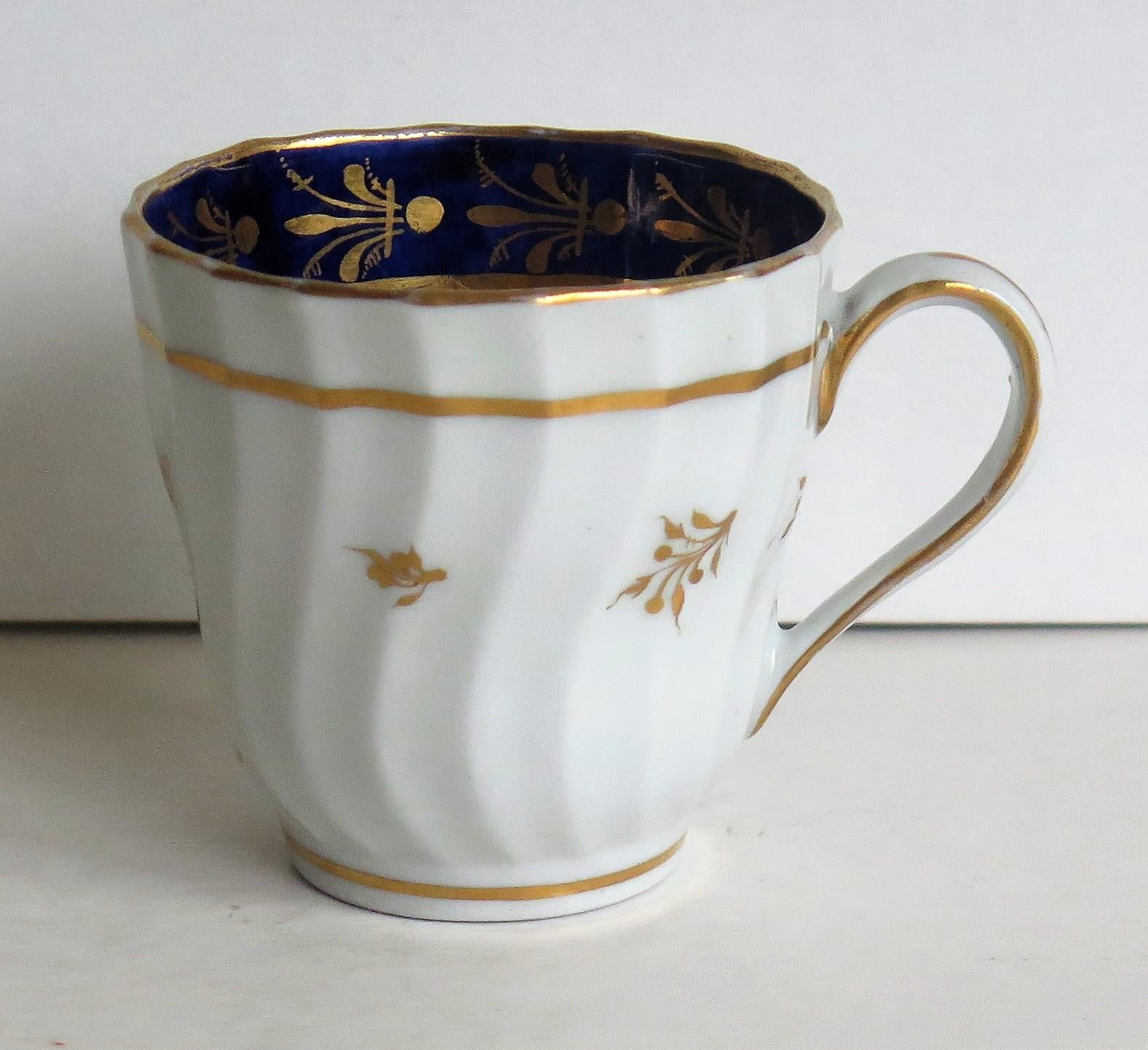 This is an early porcelain coffee cup with a shanked and Fluted Body that we attribute to the New Hall Porcelain Works of Shelton, Staffordshire, England, made, circa 1795.

The cup sits on a low foot and has a slightly waisted body which has