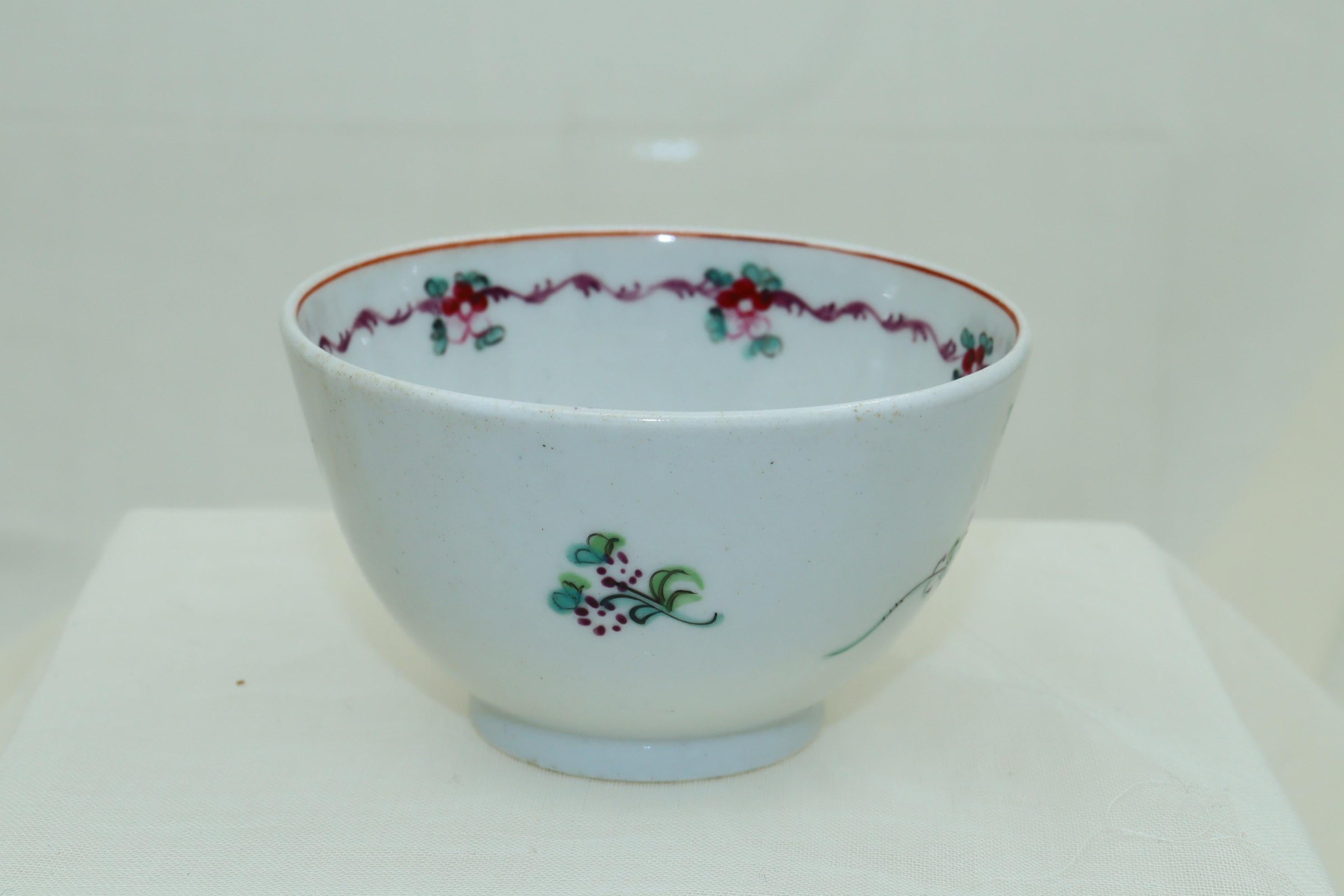 This New Hall porcelain tea bowl is decorated on the outside with a main floral spray of a large rose, a rosebud and smaller flowers together with three other smaller depictions of flowers. On the inside is an iron red line to the rim, below which