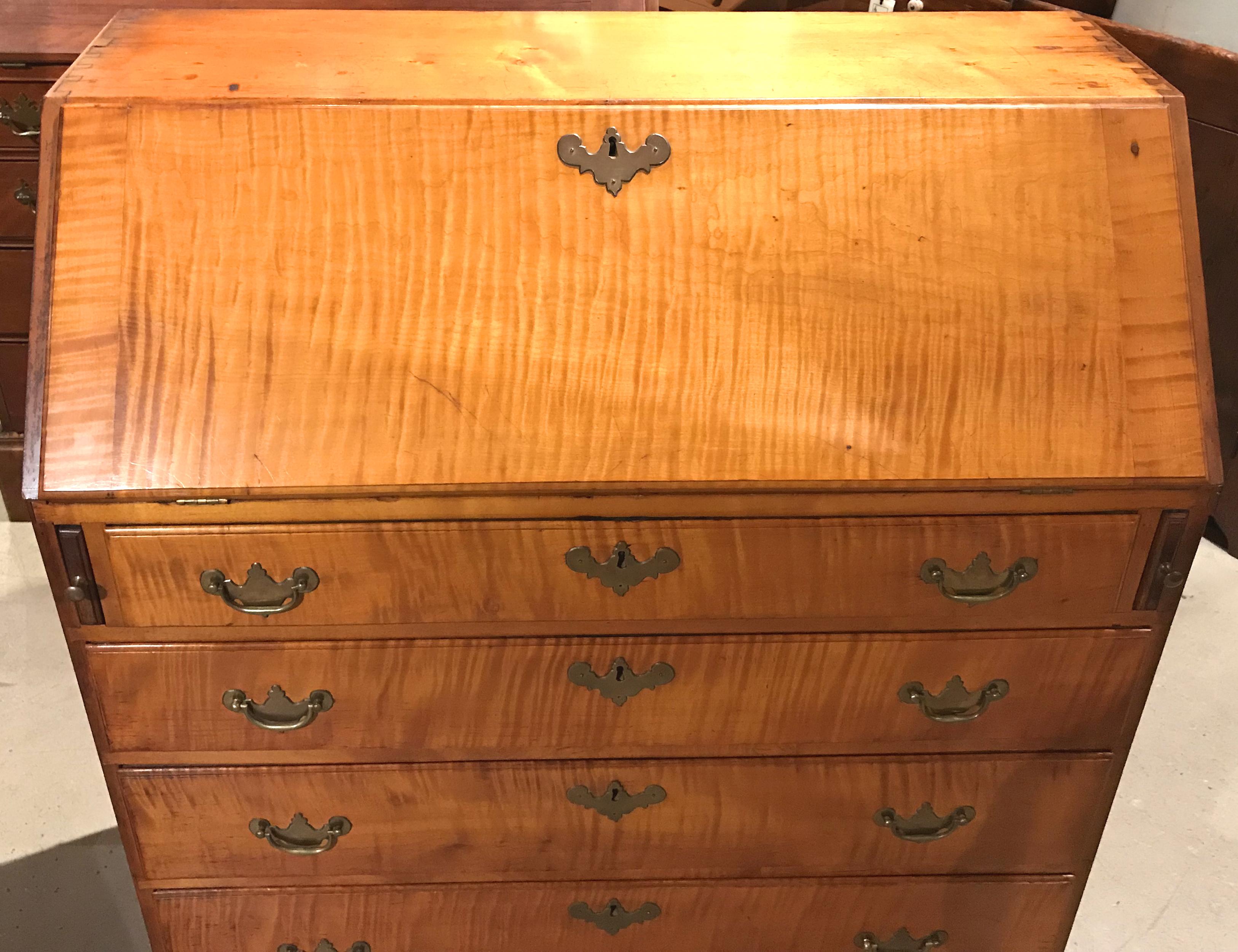 A fine example of a Chippendale style tiger maple slant top or fall front desk with compartmentalized interior, including a centre drawer with pinwheel carving, flanked by three balanced cubbies on each side over three fitted drawers. The lower case