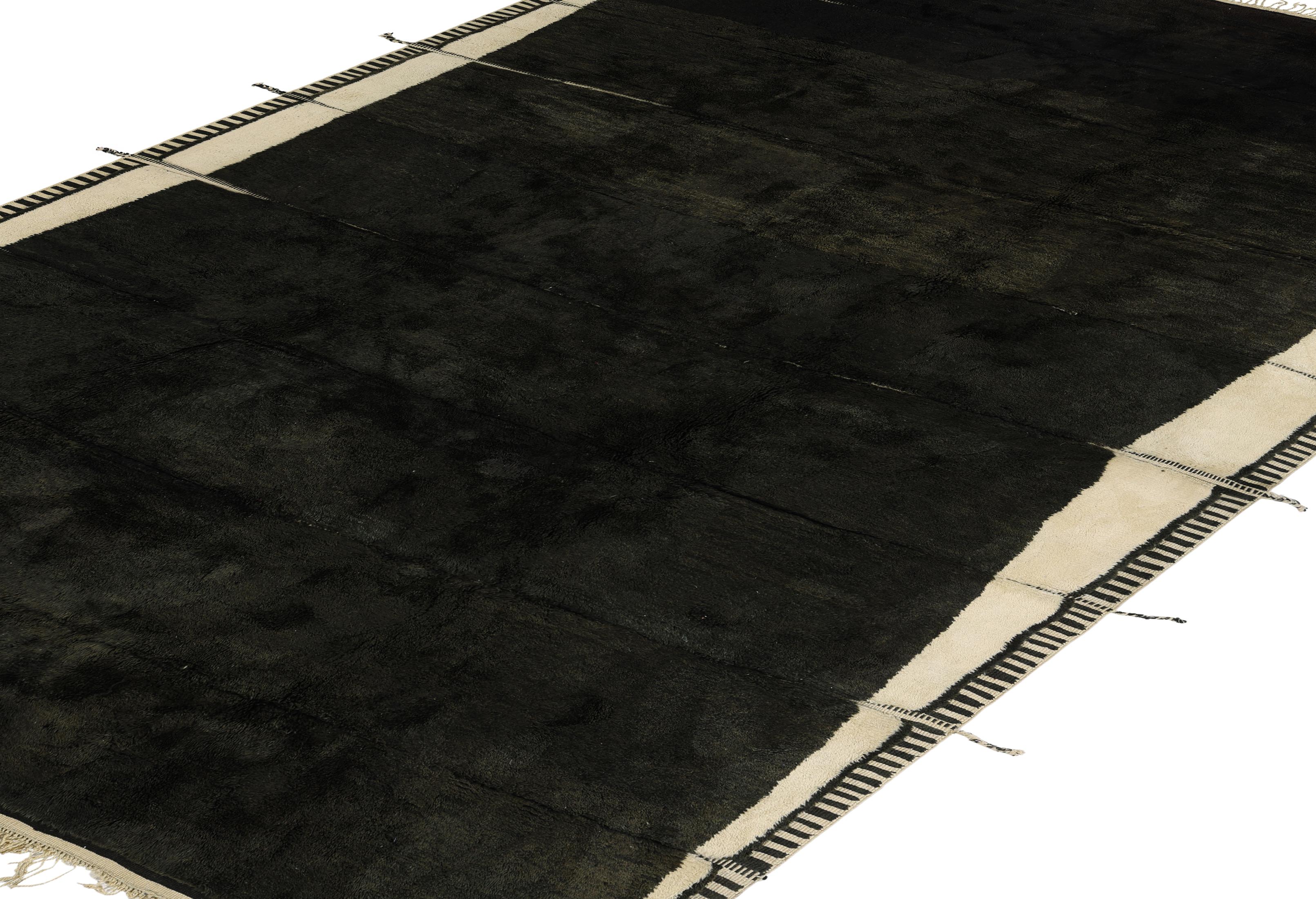 Ce nouveau tapis marocain fait main allie le tissage traditionnel berbère à un design audacieux et moderne. Fabriqué en laine naturelle de première qualité, ce tapis présente un champ noir profond bordé d'élégants panneaux latéraux crème, rehaussés